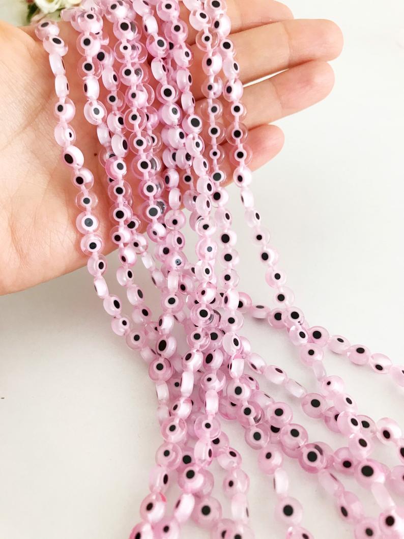 Flat round pale pink evil eye beads in various sizes from 6mm to 12mm, displayed on a white background.