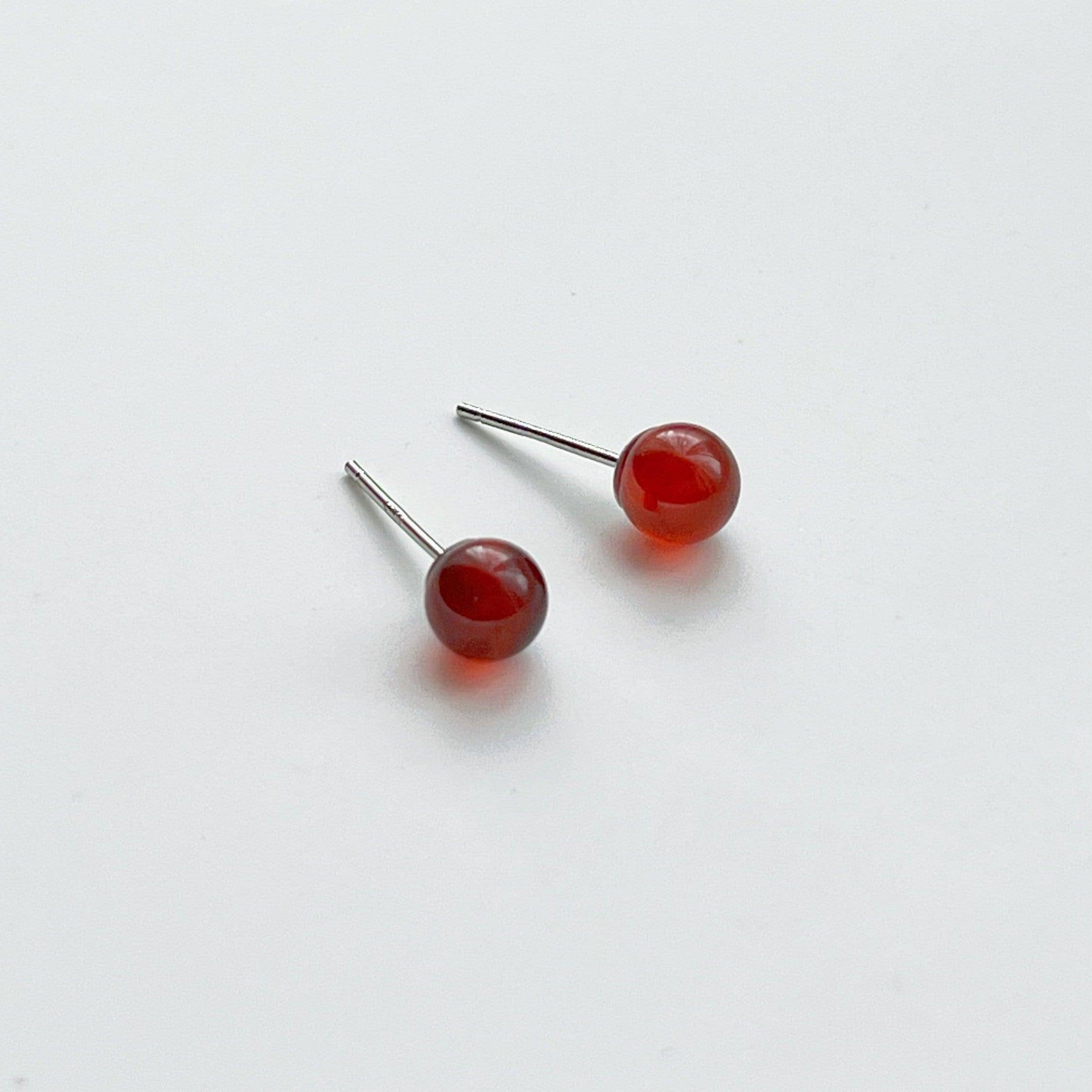 A pair of dark red garnet stud earrings set in sterling silver, showcasing their natural beauty and unique characteristics.