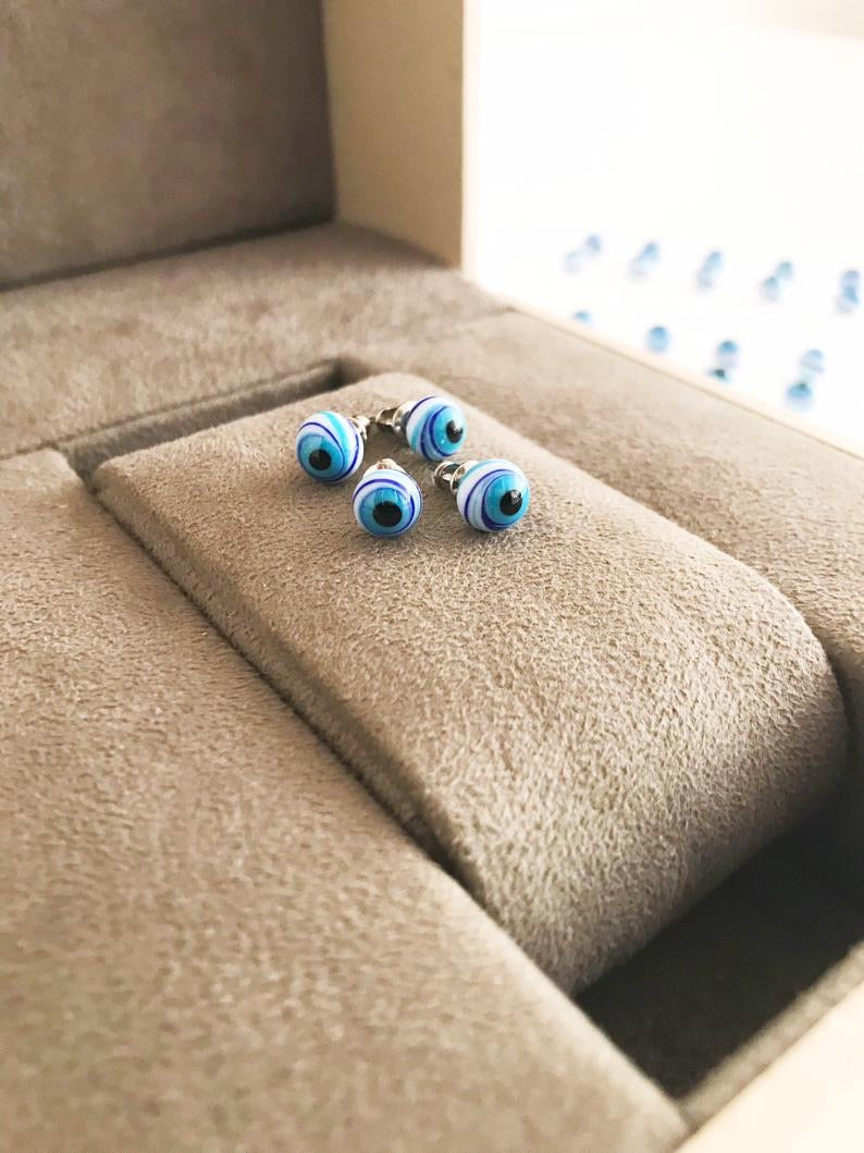 A pair of handmade Glass Evil Eye Stud Earrings featuring an 8mm blue evil eye bead with silver finishing, symbolizing protection.