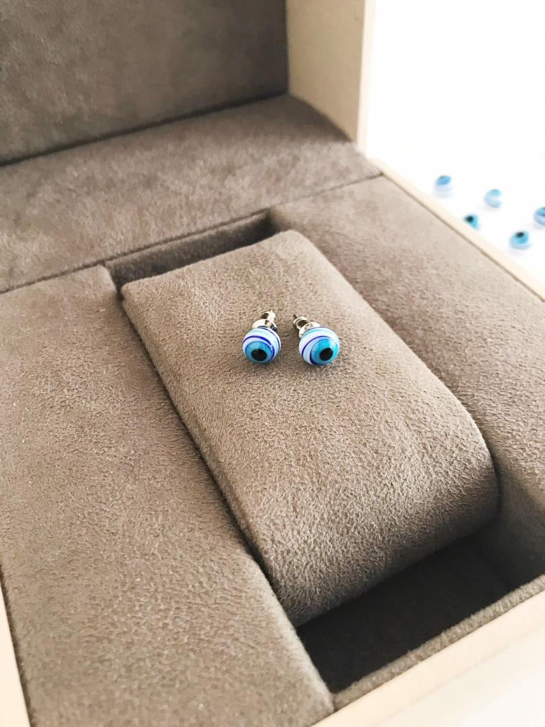 A pair of handmade Glass Evil Eye Stud Earrings featuring an 8mm blue evil eye bead with silver finishing, symbolizing protection.