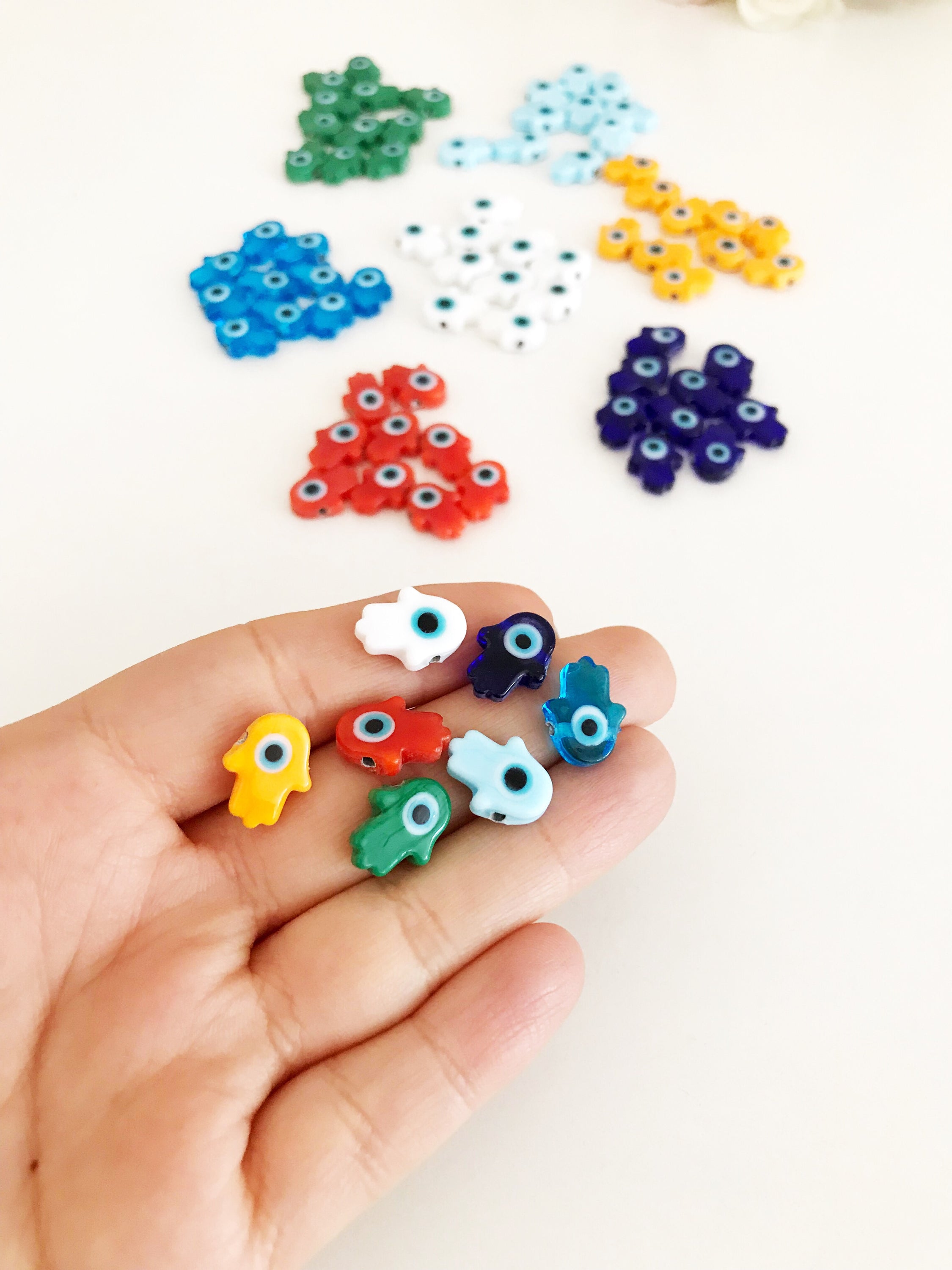 Handmade glass hamsa evil eye charm in various colors, showcasing intricate Murano glass craftsmanship.