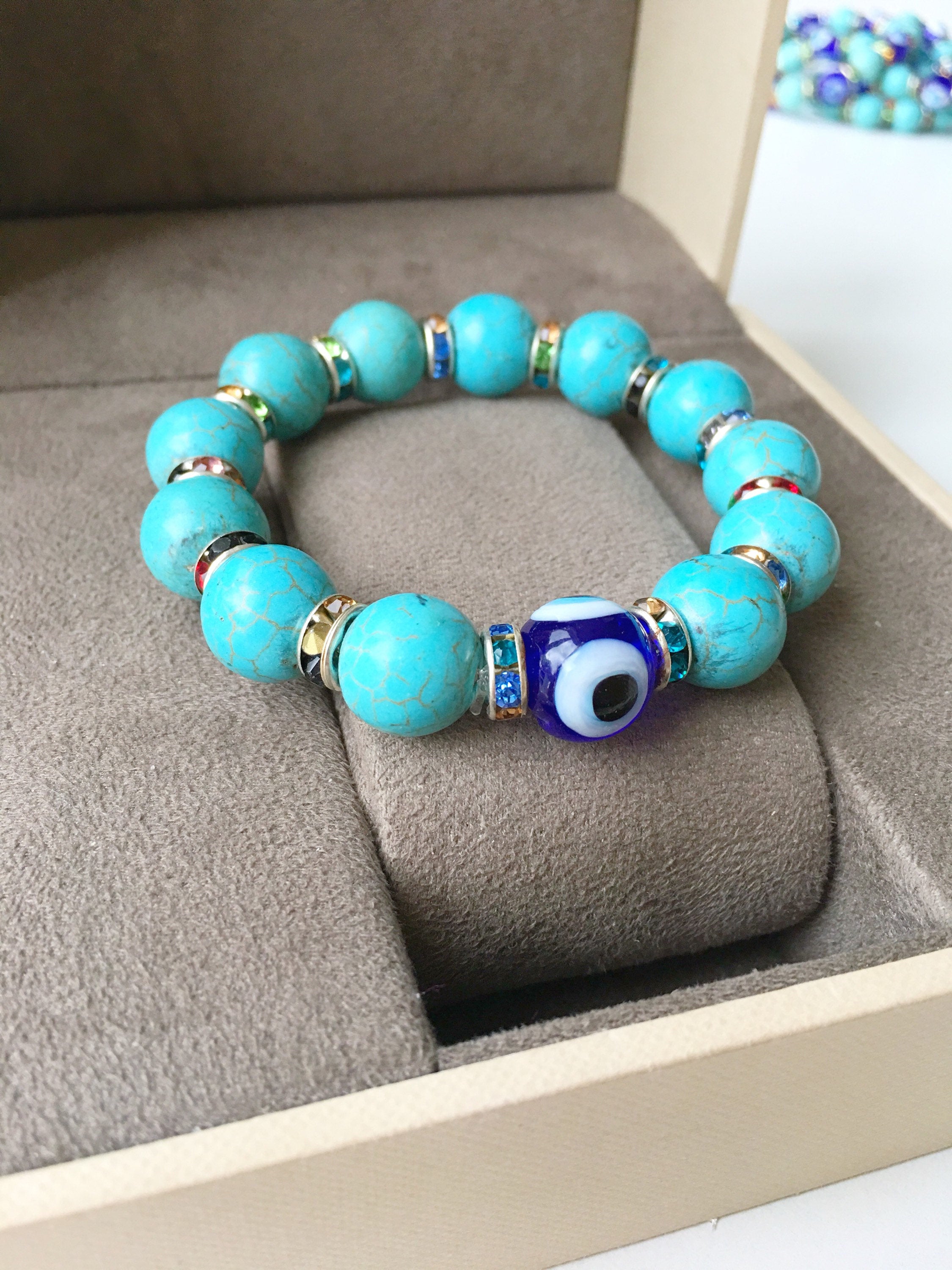 A beautiful glass turquoise bead bracelet featuring a blue evil eye charm, showcasing vibrant colors and a stretch design for comfort.