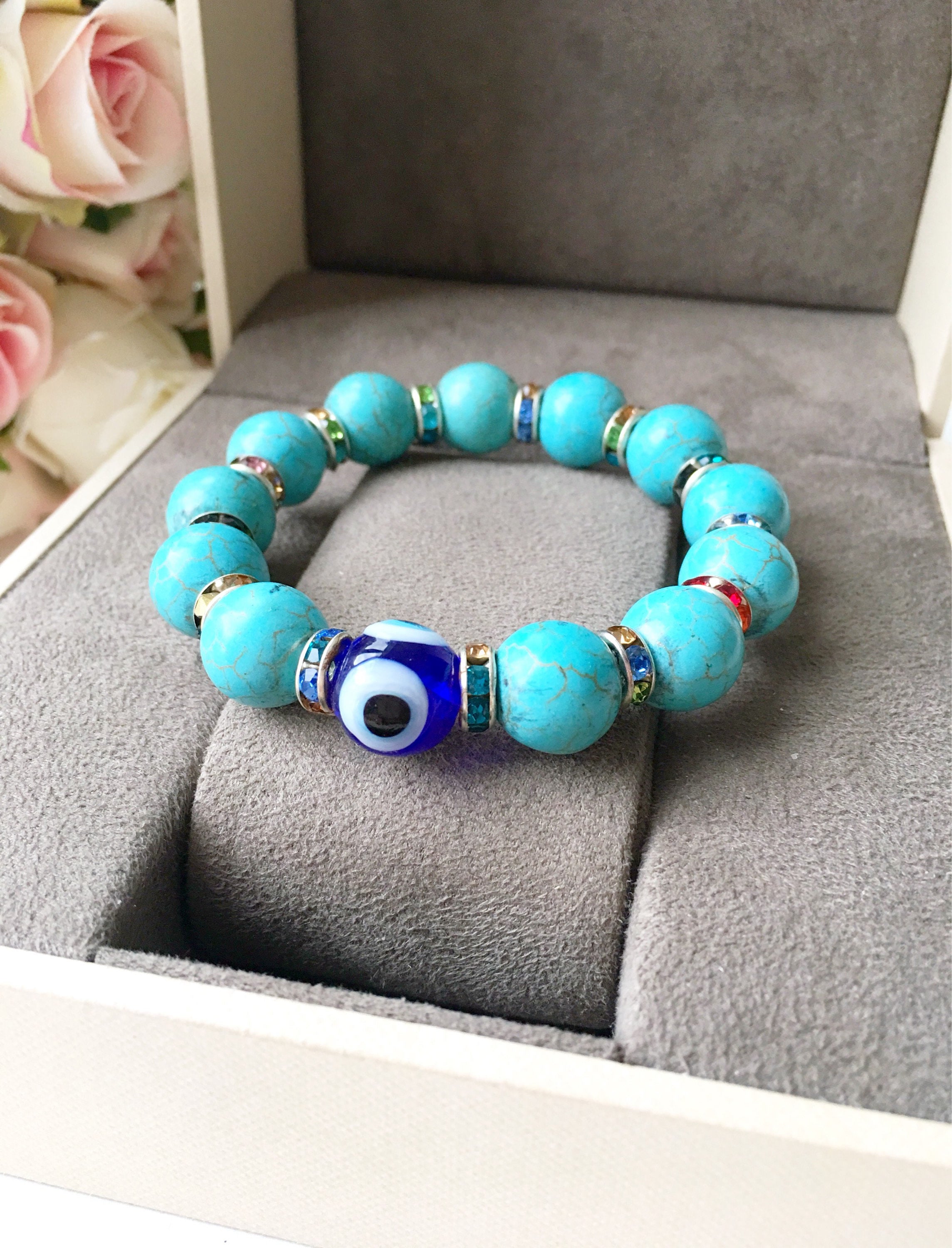 A beautiful glass turquoise bead bracelet featuring a blue evil eye charm, showcasing vibrant colors and a stretch design for comfort.