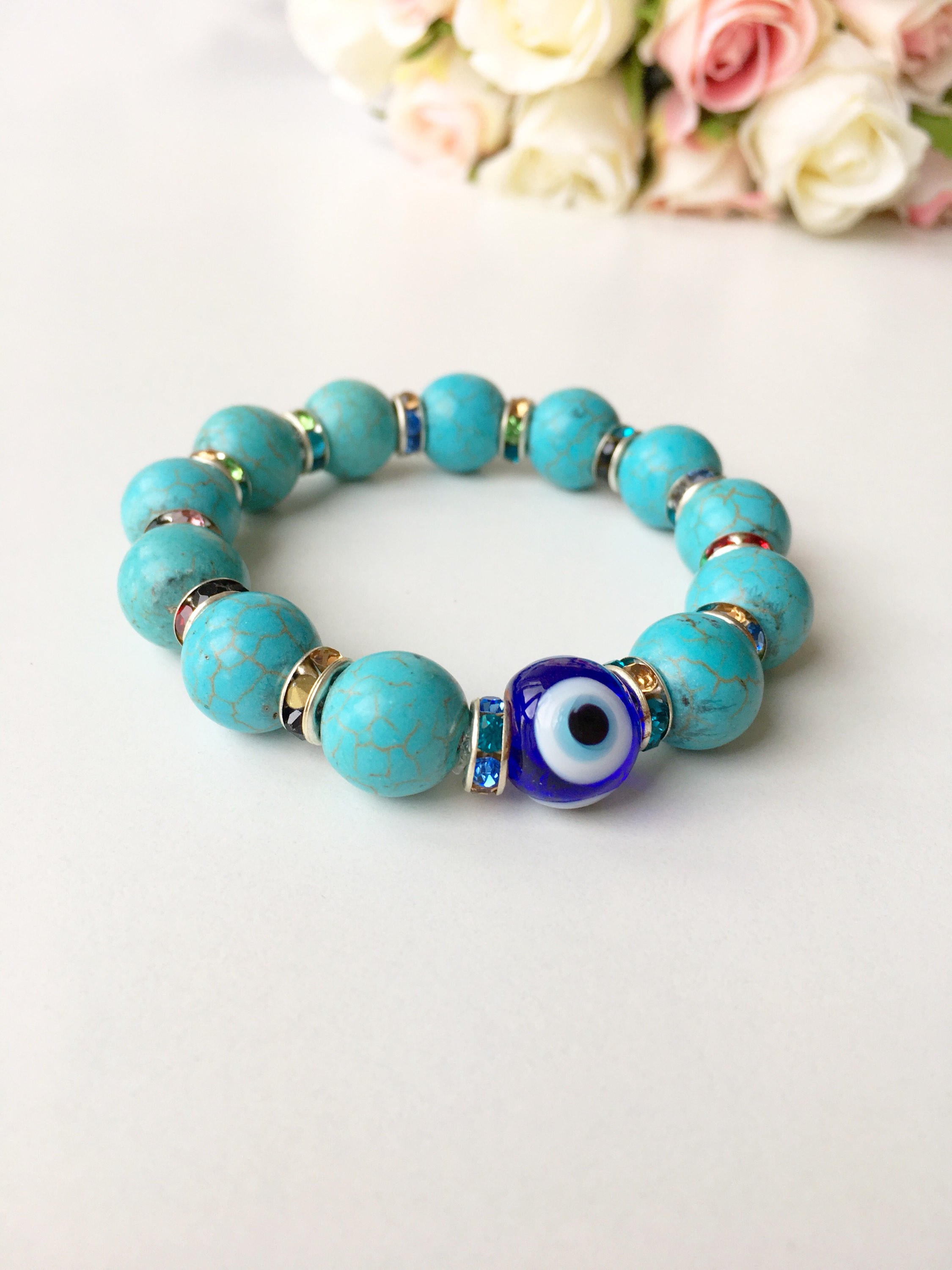 A beautiful glass turquoise bead bracelet featuring a blue evil eye charm, showcasing vibrant colors and a stretch design for comfort.