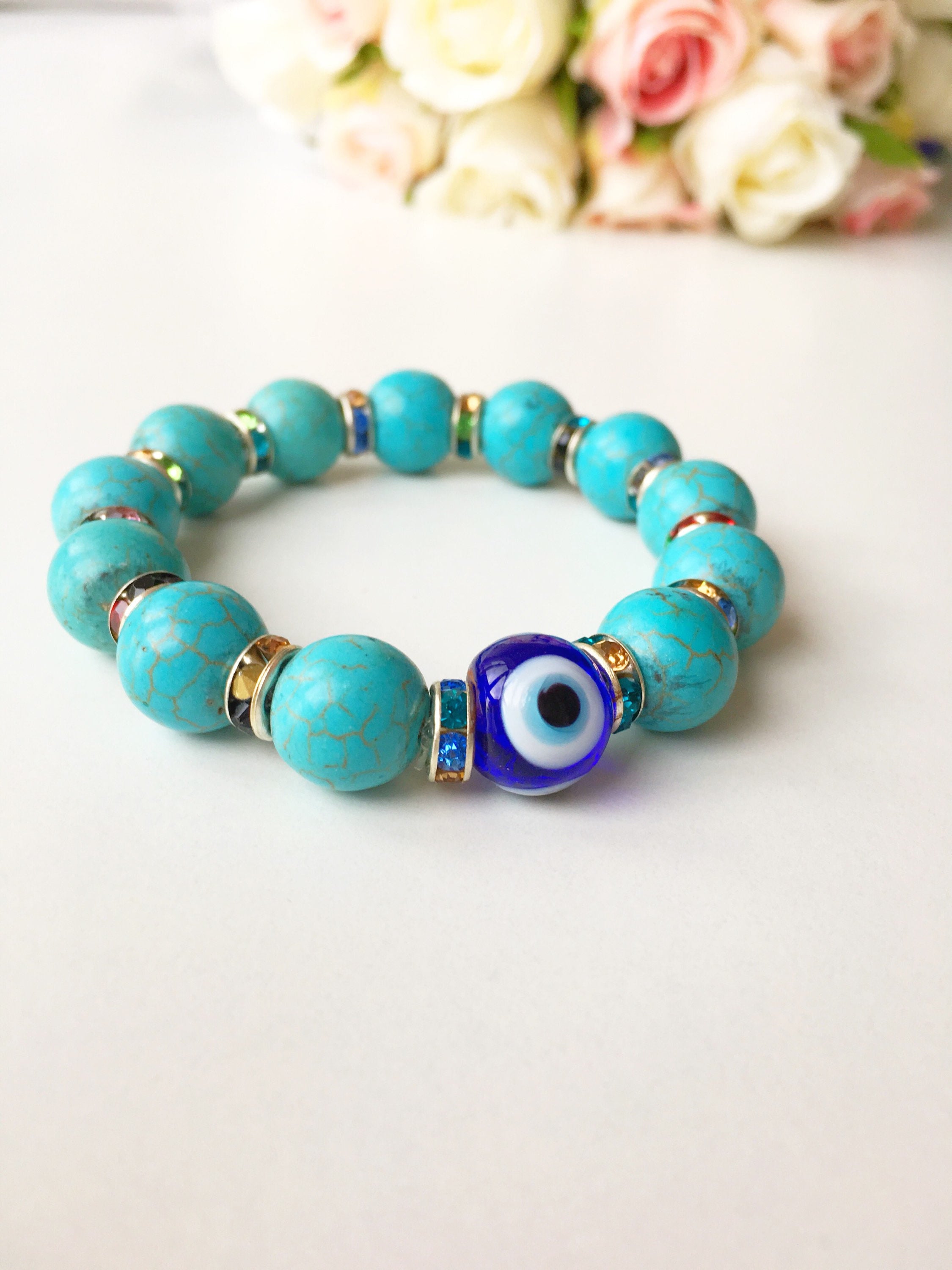 A beautiful glass turquoise bead bracelet featuring a blue evil eye charm, showcasing vibrant colors and a stretch design for comfort.