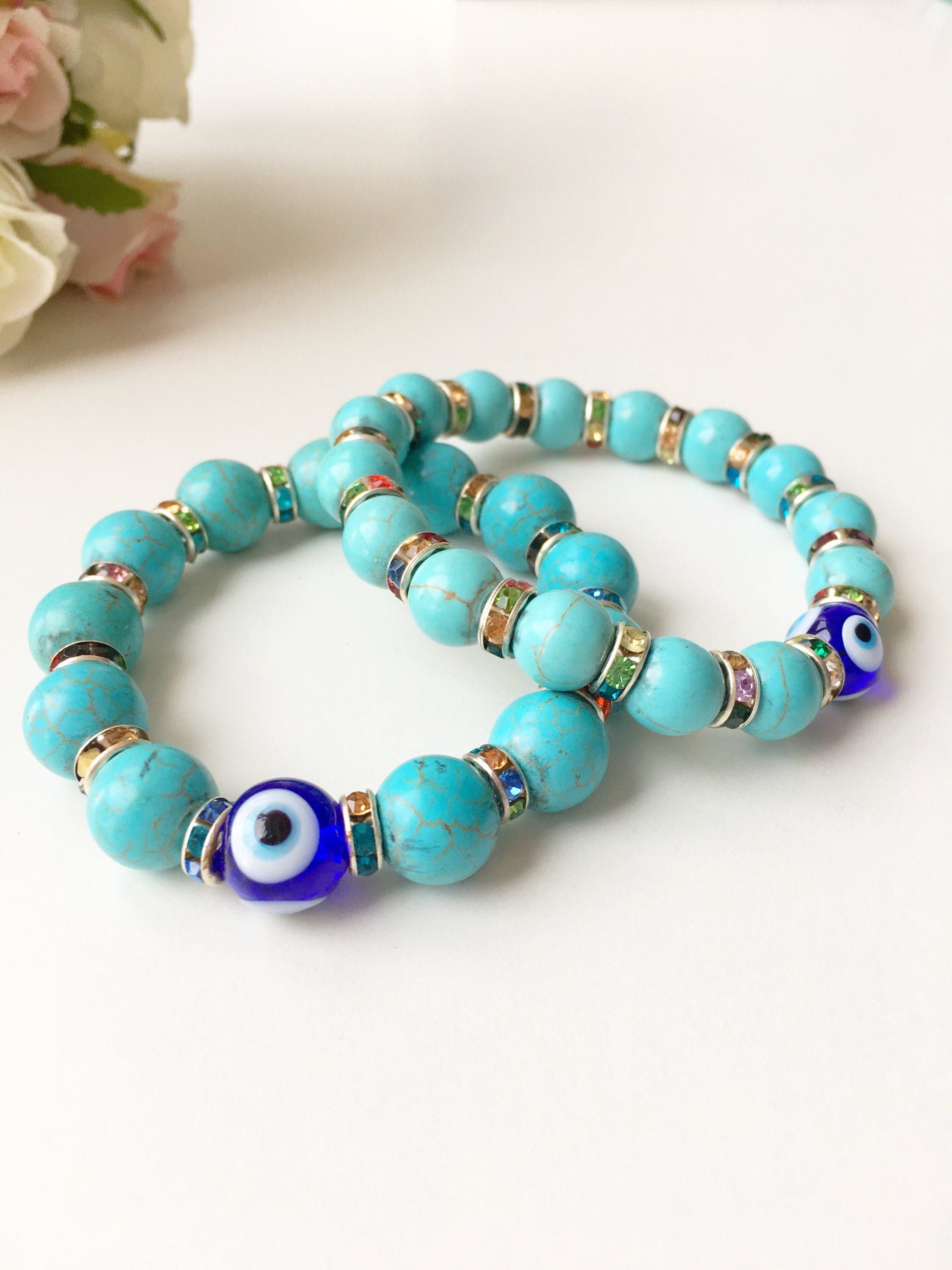 A beautiful glass turquoise bead bracelet featuring a blue evil eye charm, showcasing vibrant colors and a stretch design for comfort.