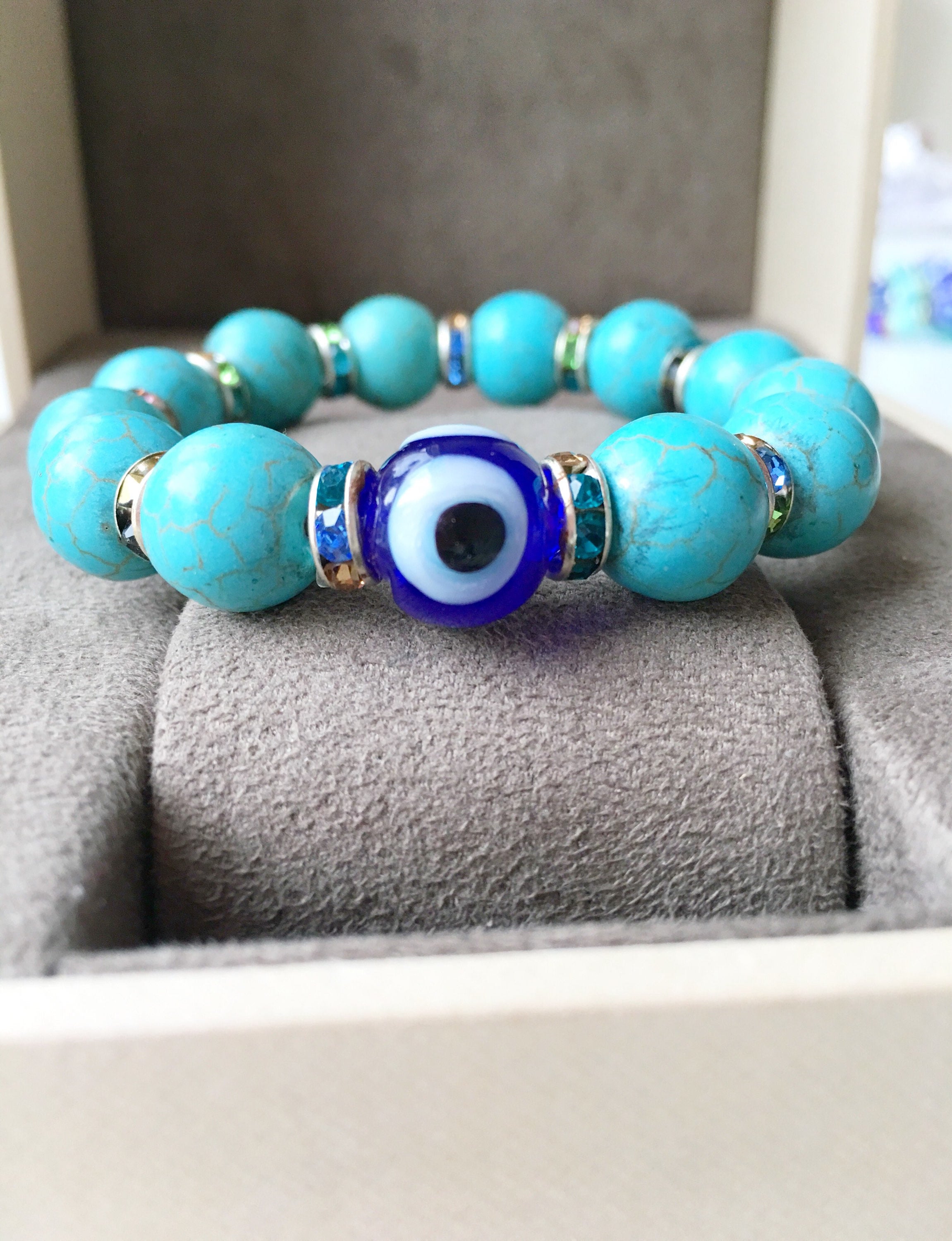 A beautiful glass turquoise bead bracelet featuring a blue evil eye charm, showcasing vibrant colors and a stretch design for comfort.