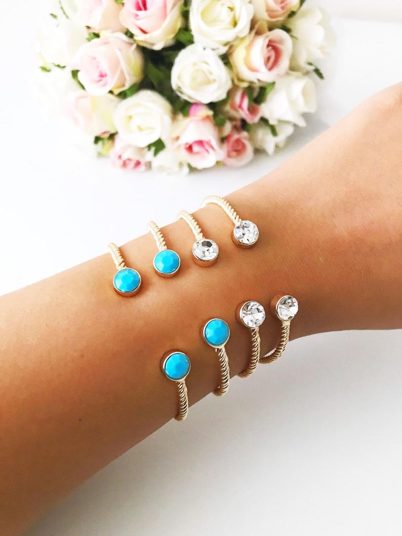 A beautiful gold bangle bracelet featuring turquoise and crystal beads, with a movable evil eye charm, showcasing its elegant design.