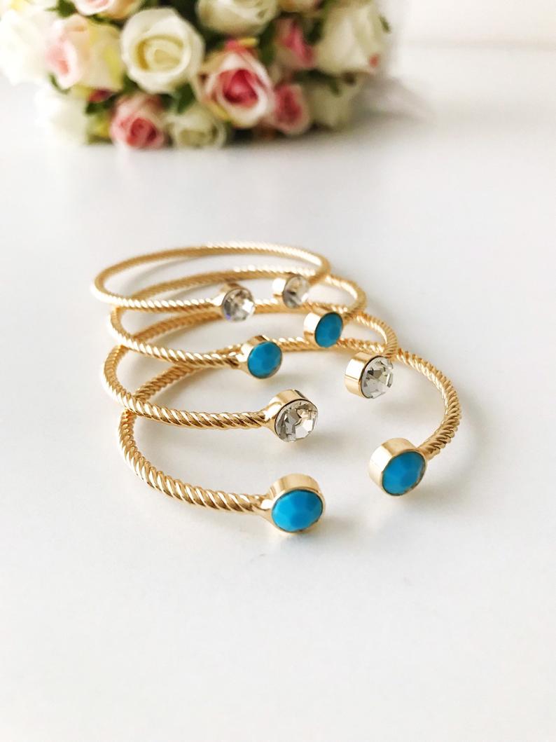 A beautiful gold bangle bracelet featuring turquoise and crystal beads, with a movable evil eye charm, showcasing its elegant design.