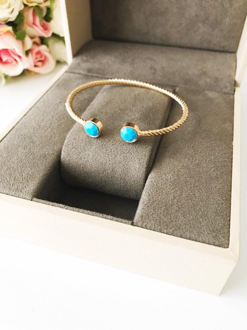 A beautiful gold bangle bracelet featuring turquoise and crystal beads, with a movable evil eye charm, showcasing its elegant design.