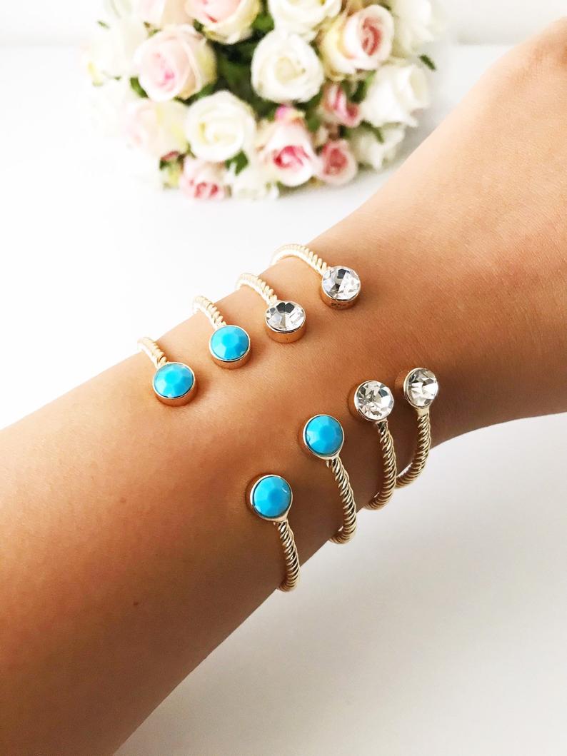 A beautiful gold bangle bracelet featuring turquoise and crystal beads, with a movable evil eye charm, showcasing its elegant design.