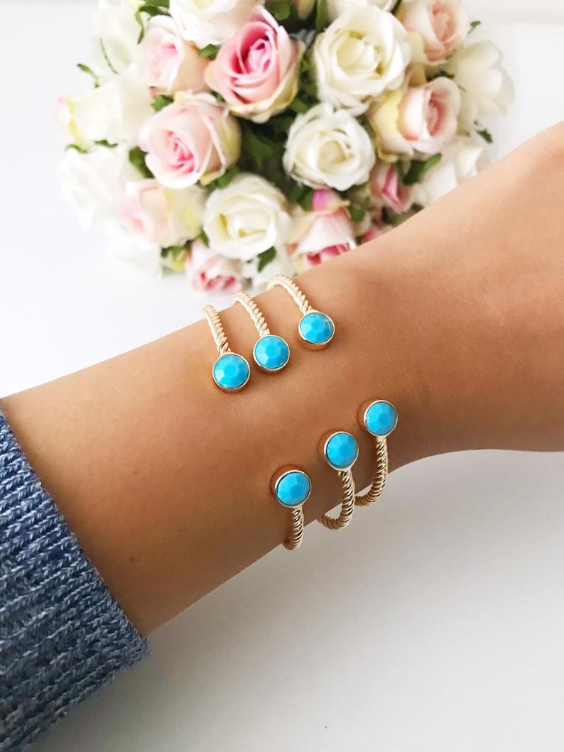A beautiful gold bangle bracelet featuring turquoise and crystal beads, with a movable evil eye charm, showcasing its elegant design.