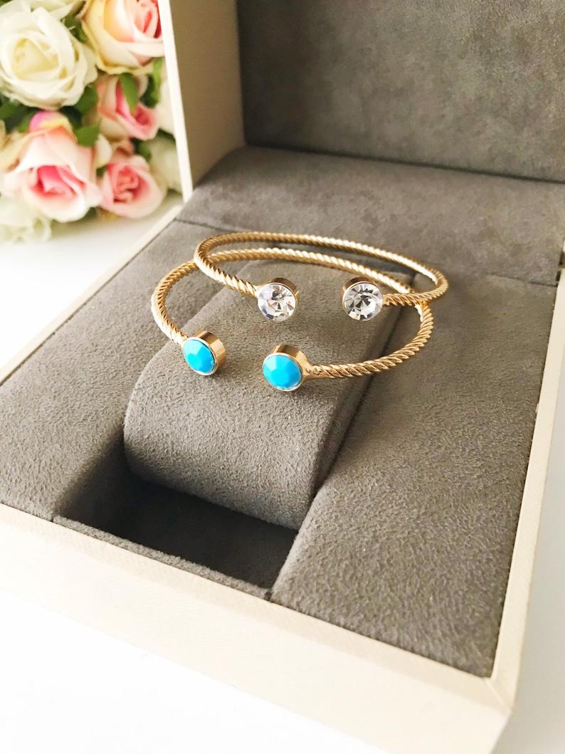 A beautiful gold bangle bracelet featuring turquoise and crystal beads, with a movable evil eye charm, showcasing its elegant design.