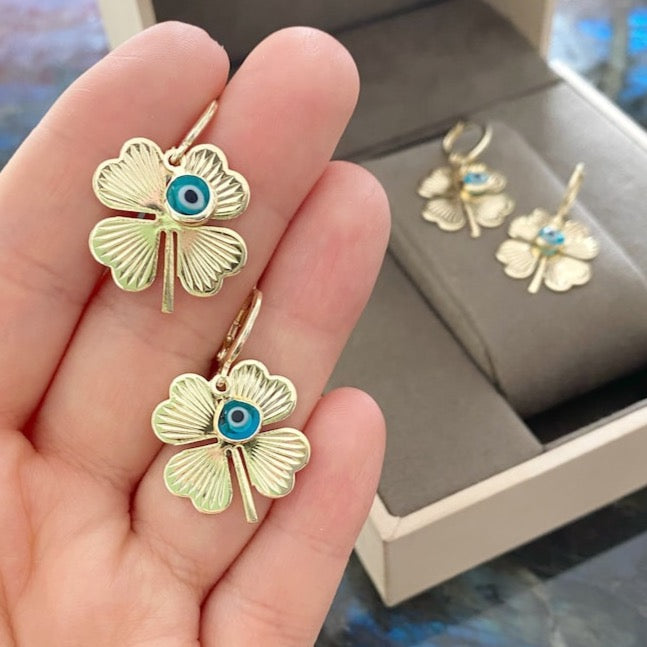 A pair of handmade gold clover hoop earrings featuring blue evil eye beads, symbolizing protection and good luck.