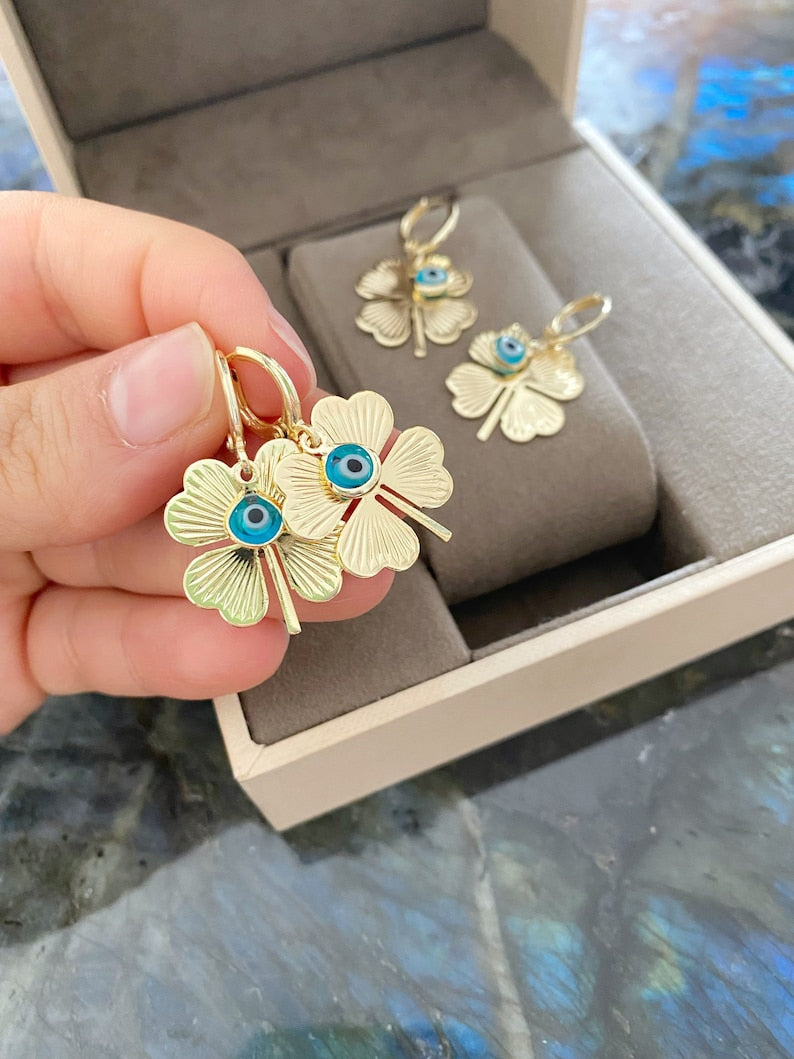 A pair of handmade gold clover hoop earrings featuring blue evil eye beads, symbolizing protection and good luck.