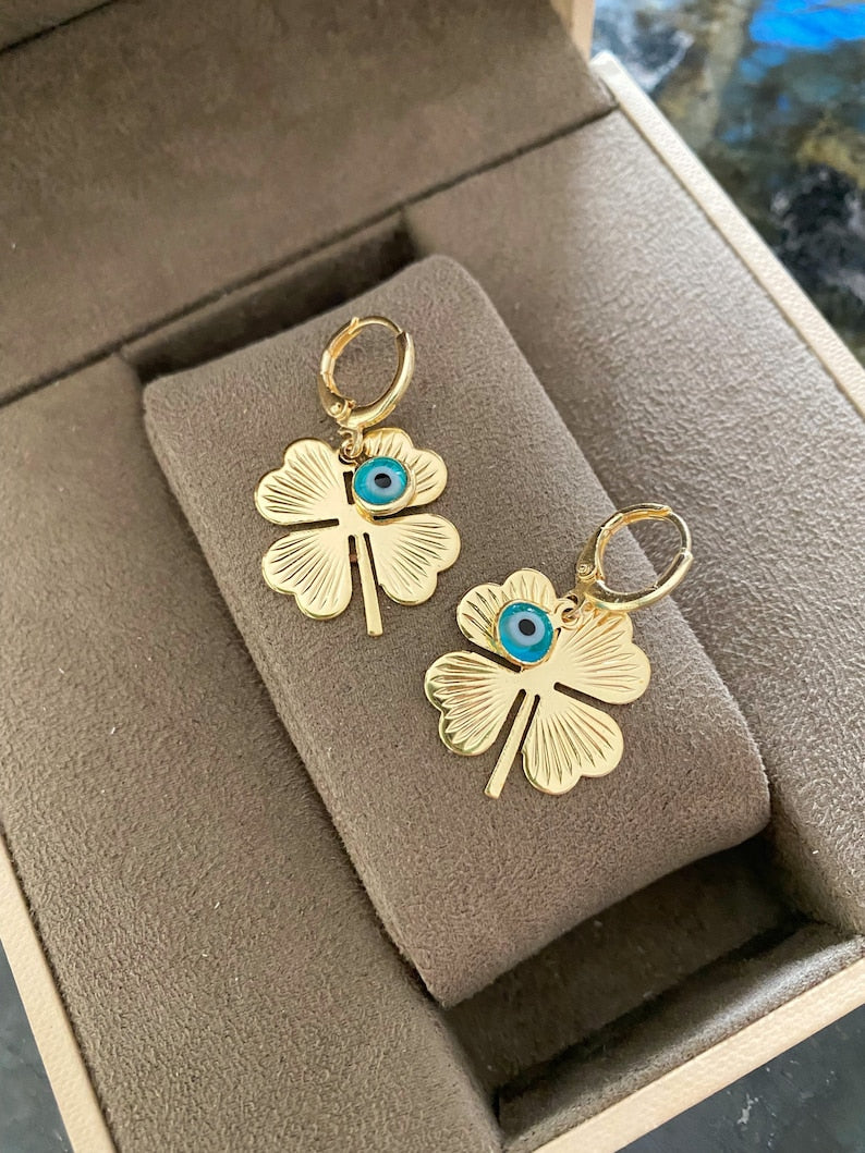 A pair of handmade gold clover hoop earrings featuring blue evil eye beads, symbolizing protection and good luck.