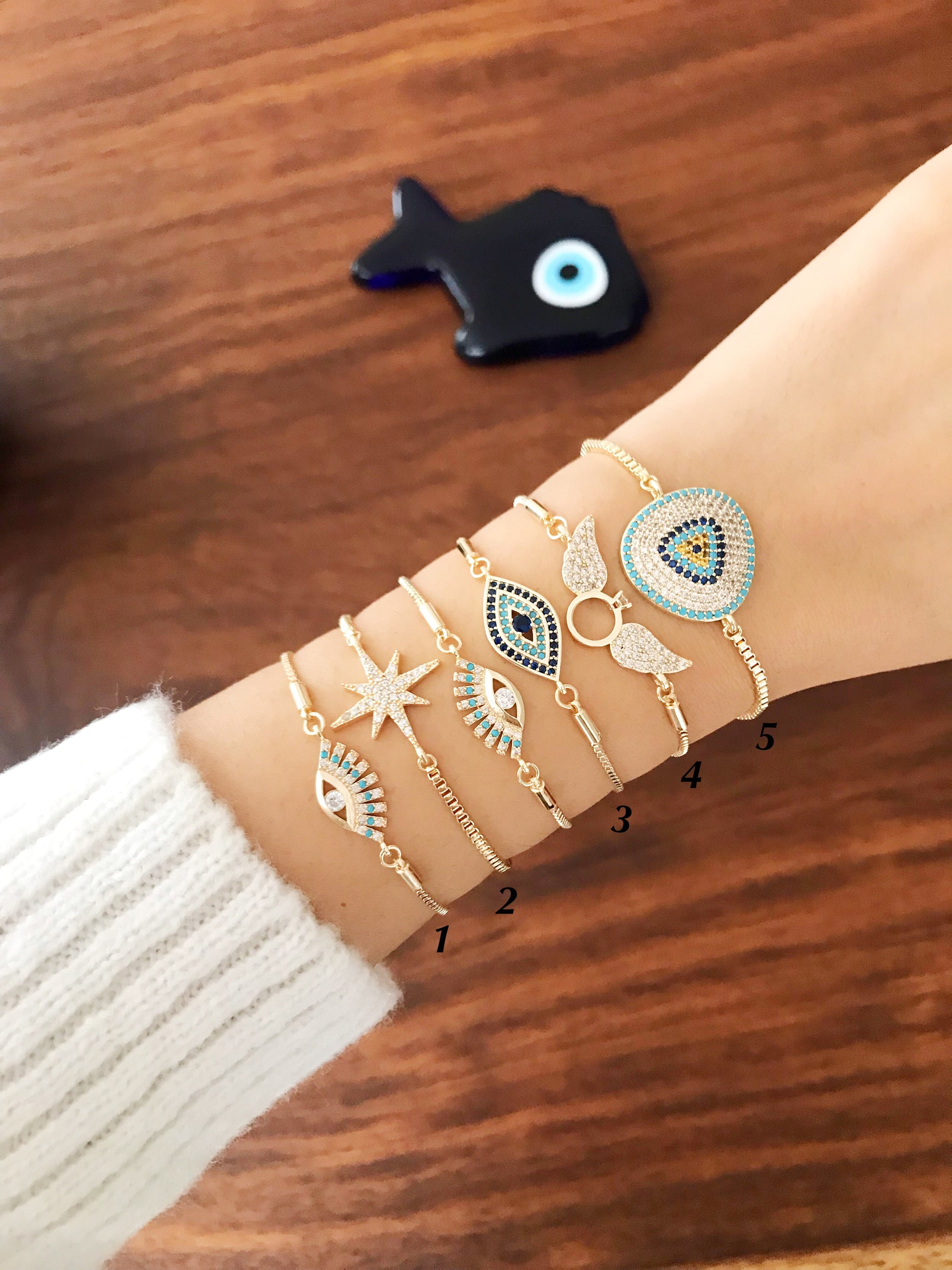 A collection of gold evil eye adjustable bracelets featuring turquoise beads, zircon, and angel wings designs, showcasing their handmade craftsmanship.