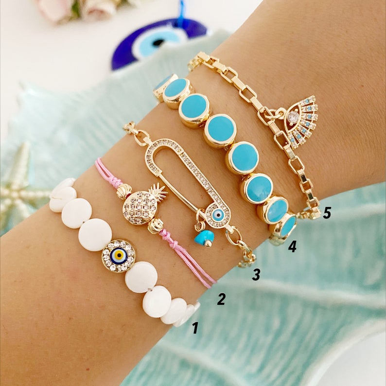 Gold Evil Eye Bracelet featuring turquoise beads and a safety pin design, showcasing its handmade craftsmanship and adjustable fit.