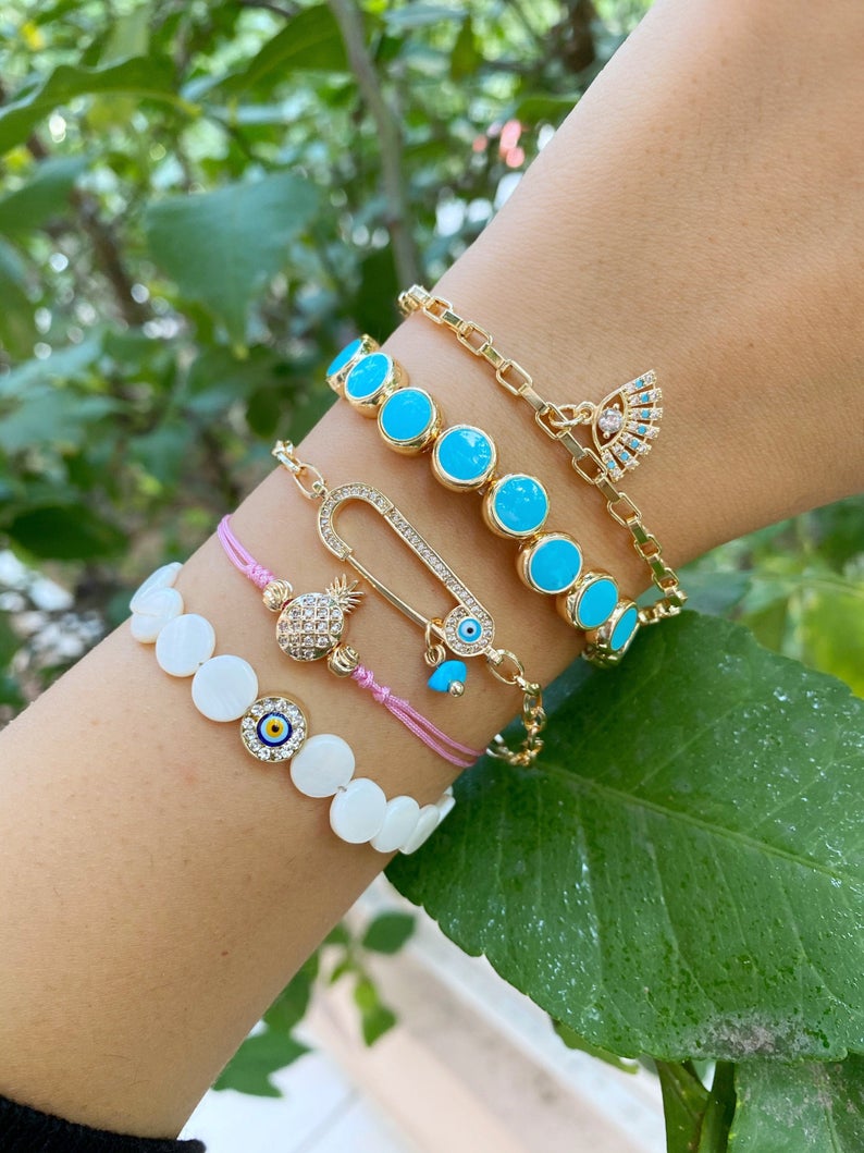 Gold Evil Eye Bracelet featuring turquoise beads and a safety pin design, showcasing its handmade craftsmanship and adjustable fit.