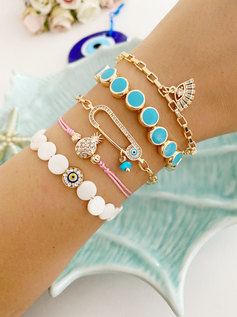 Gold Evil Eye Bracelet featuring turquoise beads and a safety pin design, showcasing its handmade craftsmanship and adjustable fit.