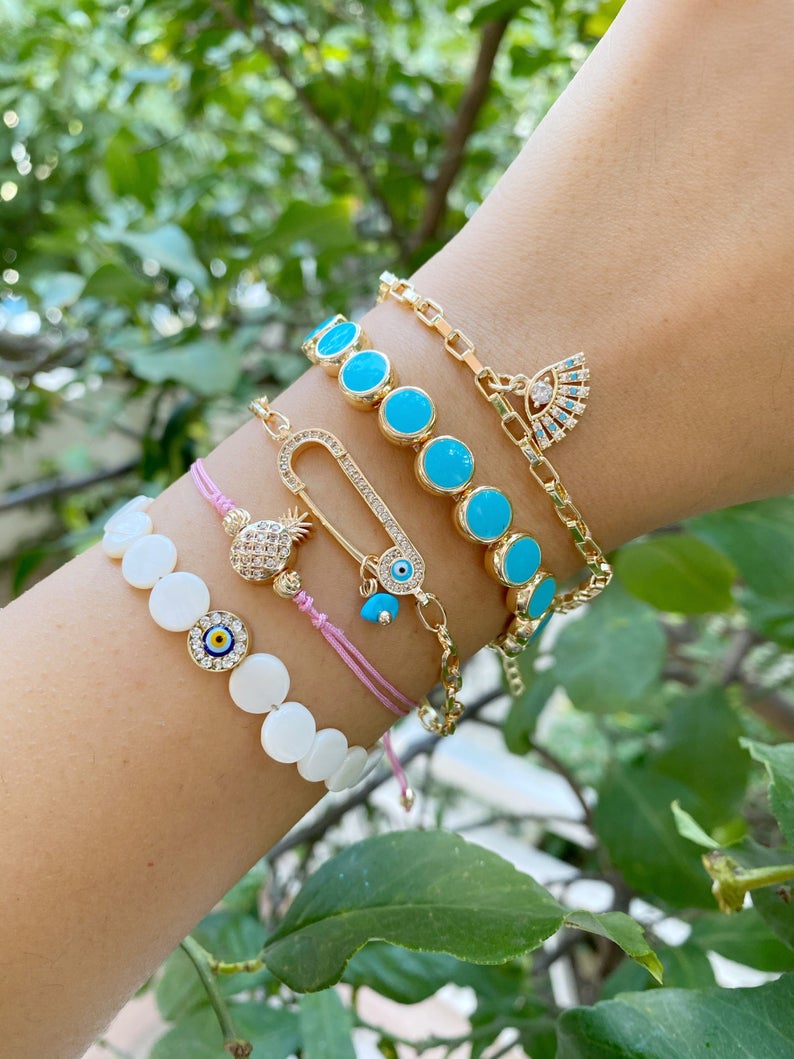 Gold Evil Eye Bracelet featuring turquoise beads and a safety pin design, showcasing its handmade craftsmanship and adjustable fit.