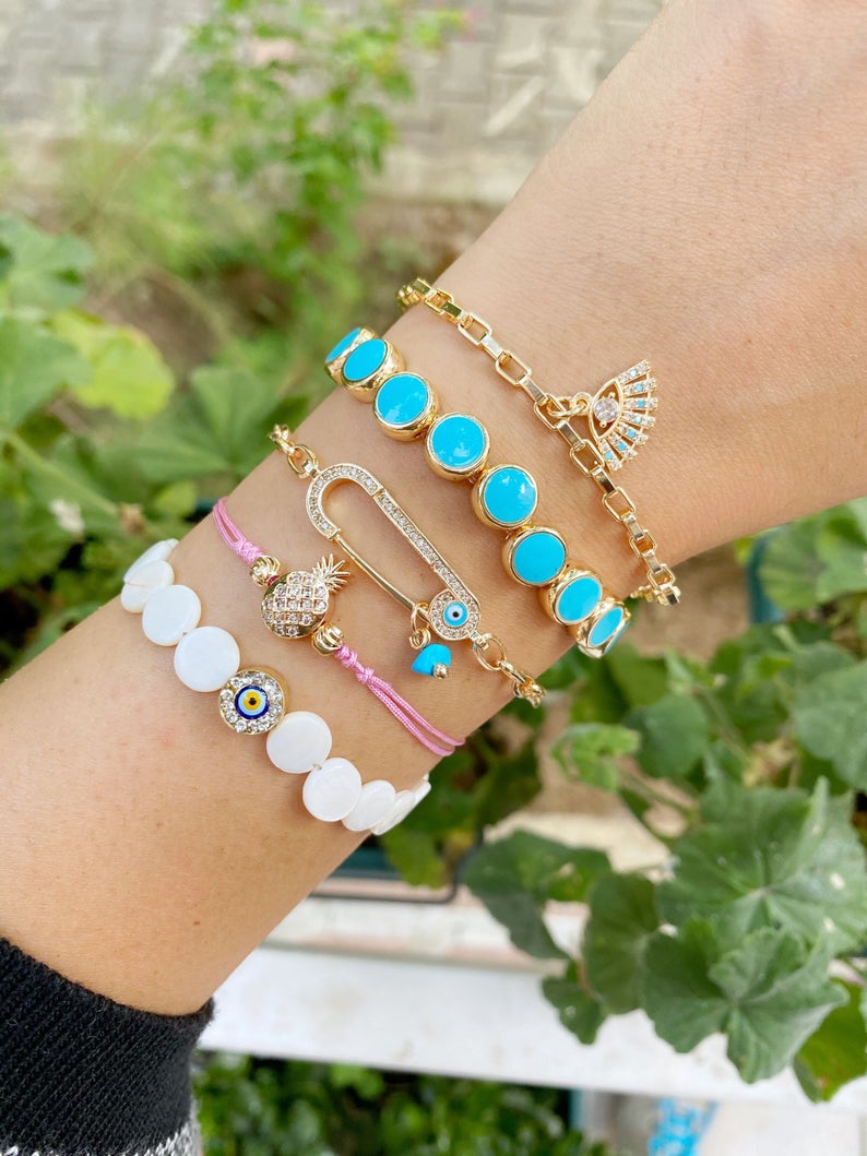 Gold Evil Eye Bracelet featuring turquoise beads and a safety pin design, showcasing its handmade craftsmanship and adjustable fit.