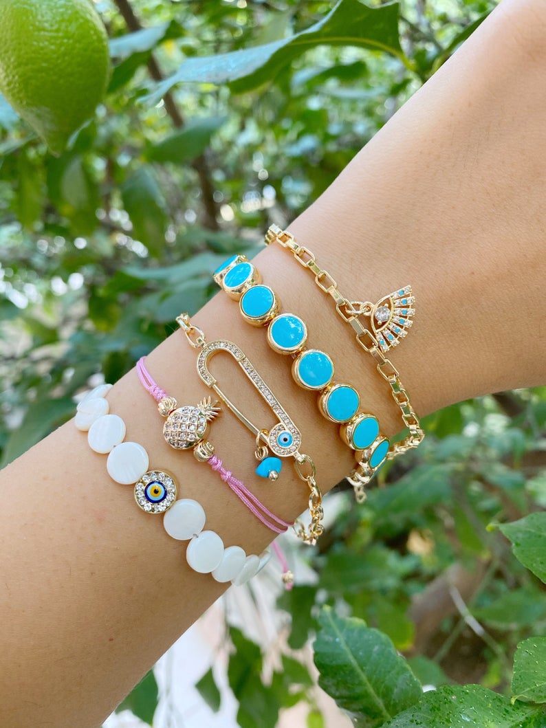 Gold Evil Eye Bracelet featuring turquoise beads and a safety pin design, showcasing its handmade craftsmanship and adjustable fit.