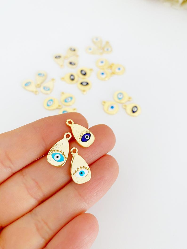 Five gold evil eye charms in round and oval shapes, featuring blue, white, and turquoise colors, ideal for DIY jewelry making.