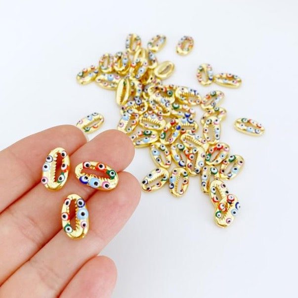 A collection of Gold Evil Eye Charms and Cowrie Shell Charms, showcasing their intricate designs and 24K gold plating.