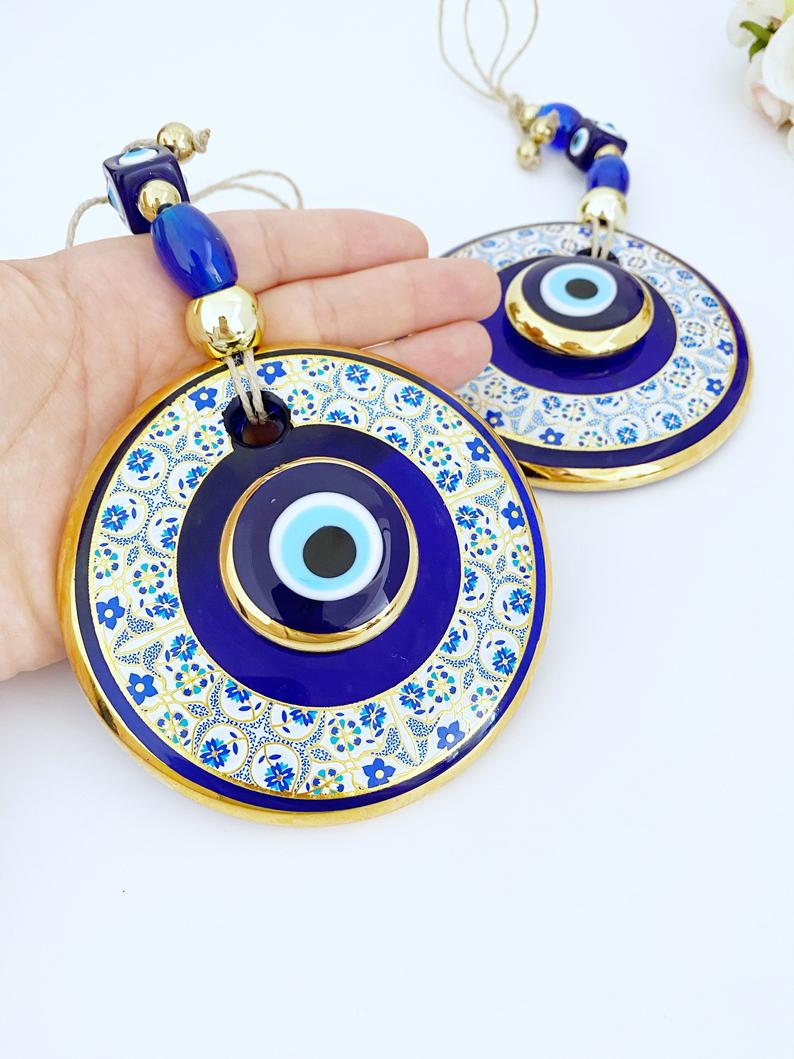 Gold Evil Eye Wall Hanging featuring a white patterned design, handmade with intricate details, symbolizing protection and good fortune.