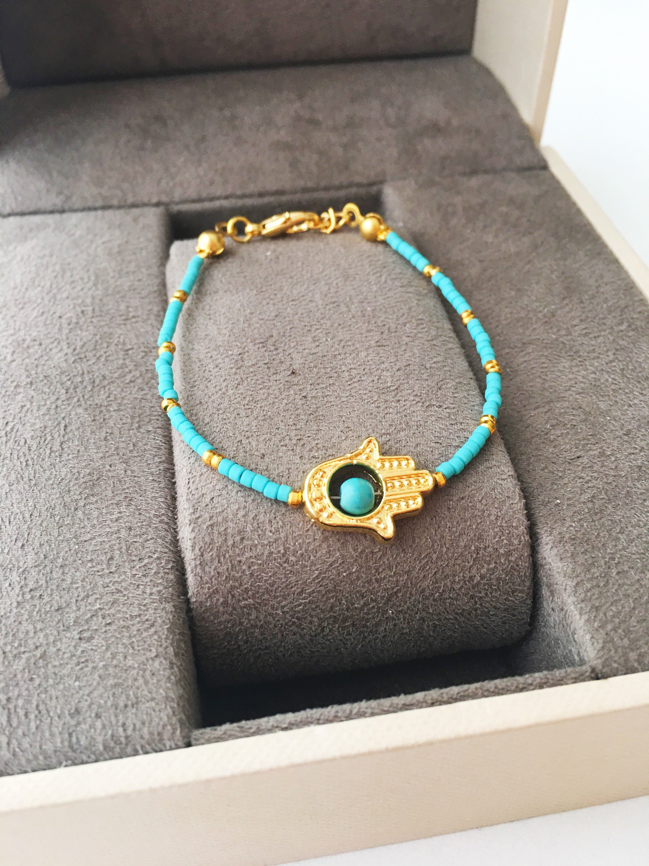 Gold Hamsa Hand Bracelet featuring colorful seed beads and a turquoise bead design, symbolizing luck and protection.