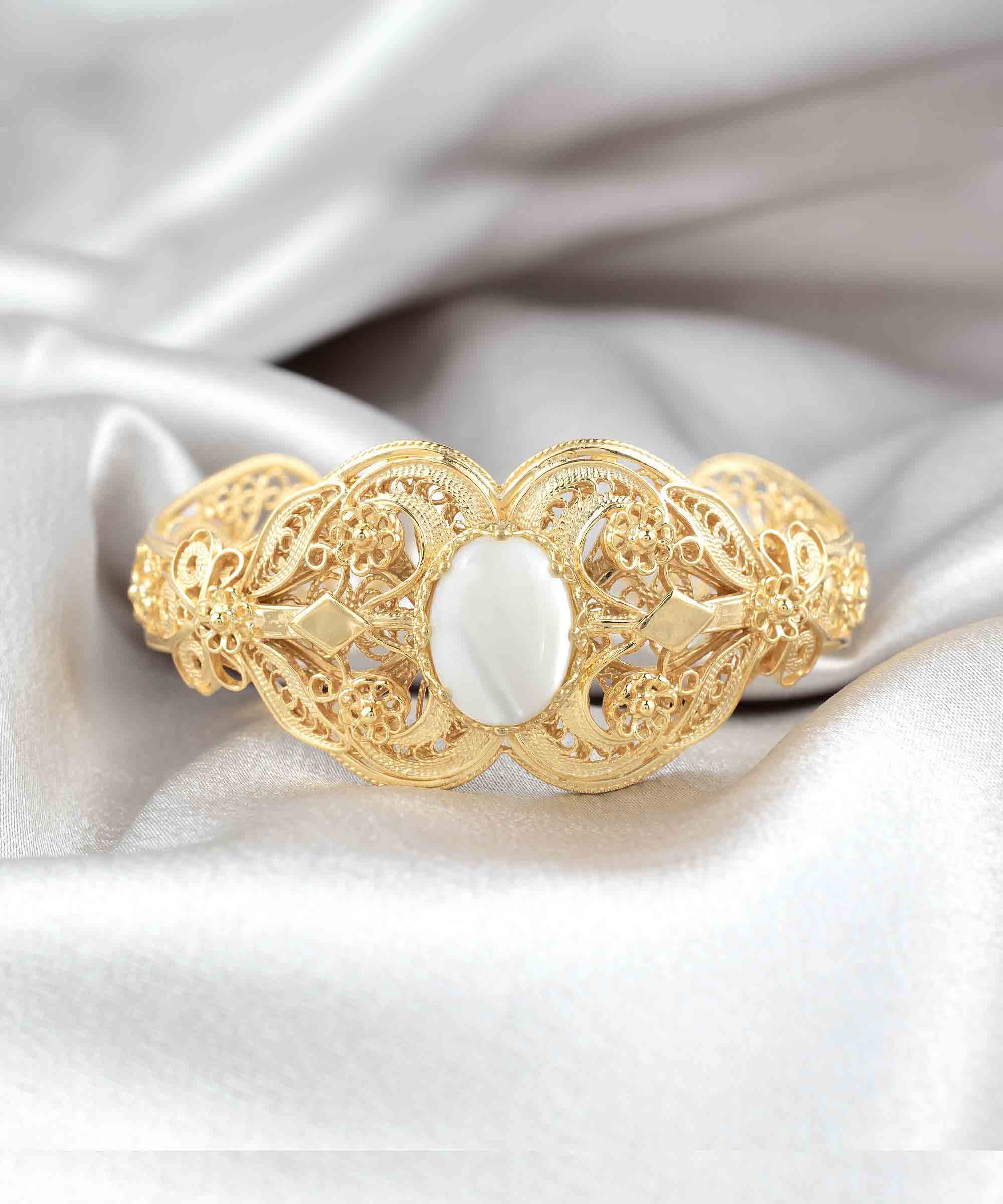 Gold plated sterling silver cuff bracelet with intricate filigree art and a mother of pearl gemstone, elegantly displayed in a velvet pouch.