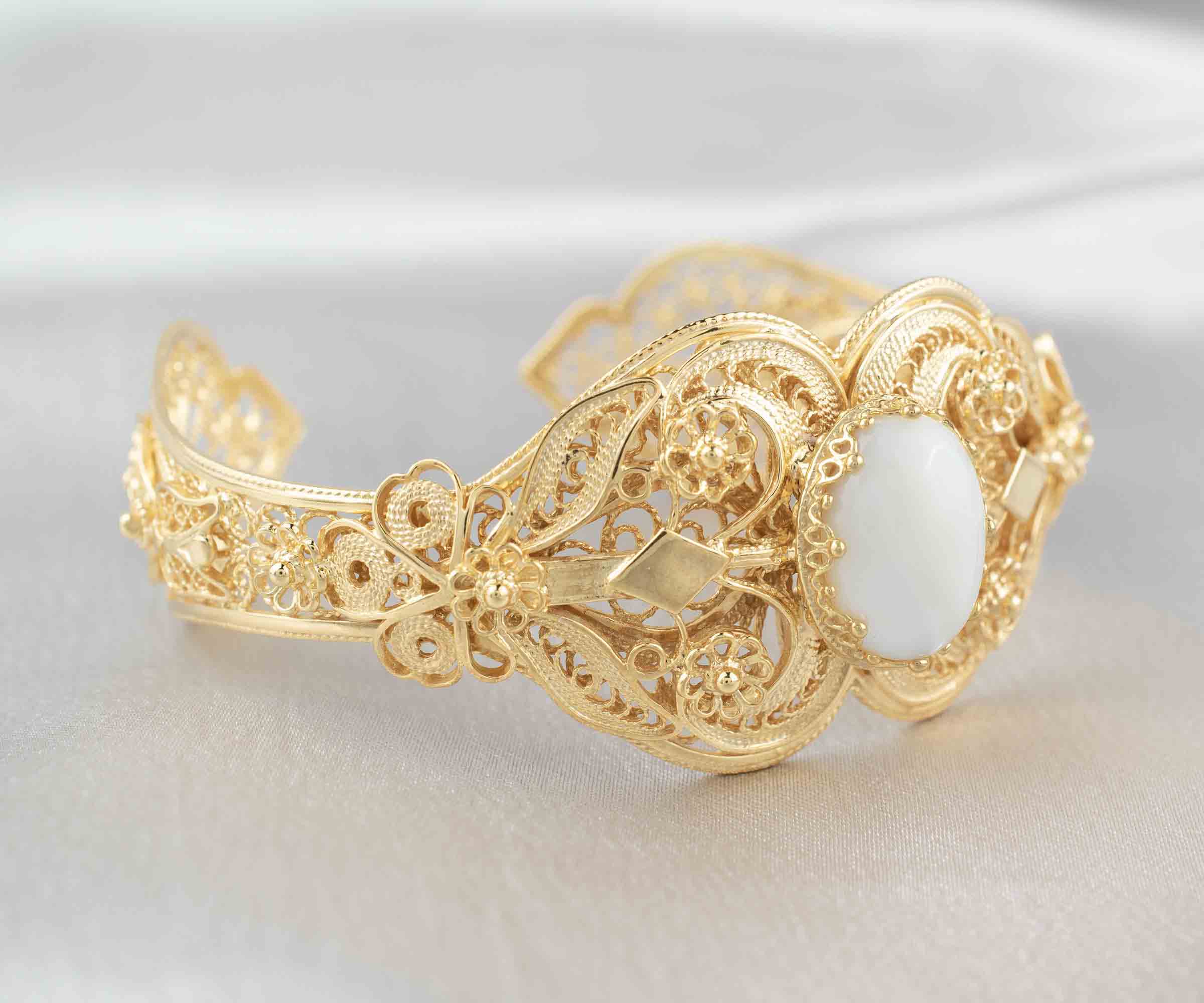 Gold plated sterling silver cuff bracelet with intricate filigree art and a mother of pearl gemstone, elegantly displayed in a velvet pouch.
