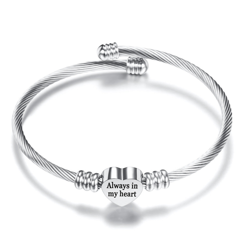 A polished stainless steel bangle featuring a heart charm with the quote 'Always in My Heart', perfect for gifting.