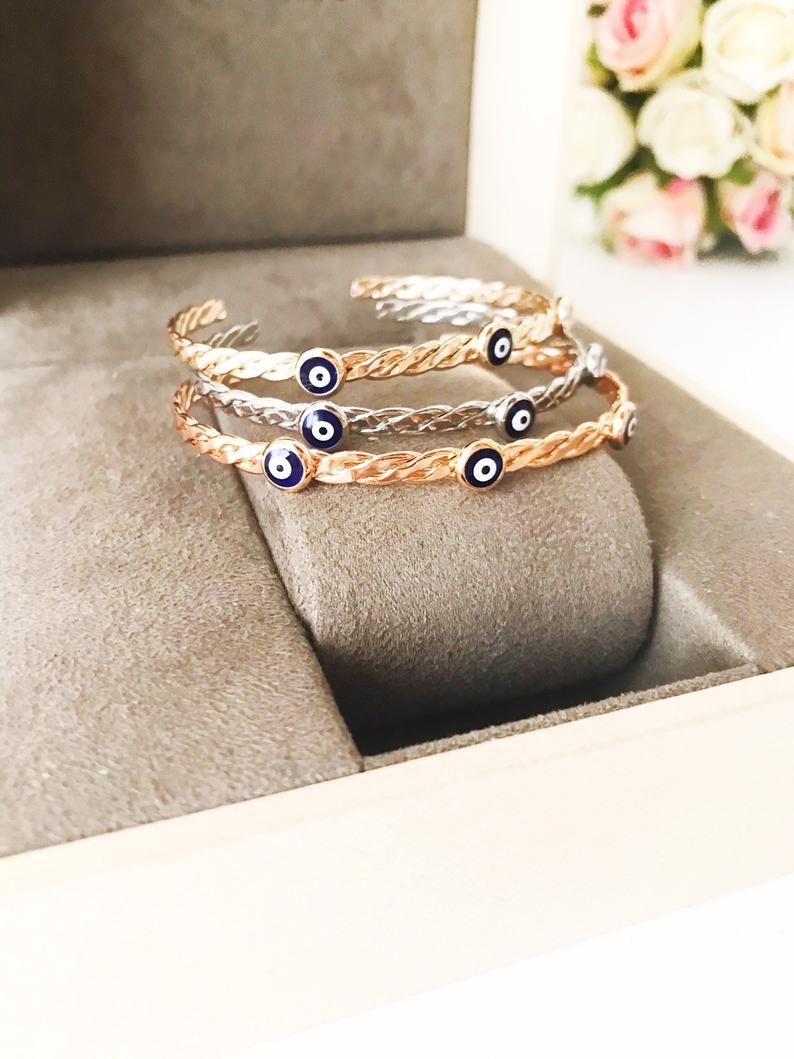 A stylish Greek Evil Eye Bracelet Set featuring a gold bangle and blue evil eye charm, showcasing its handmade craftsmanship and adjustable design.