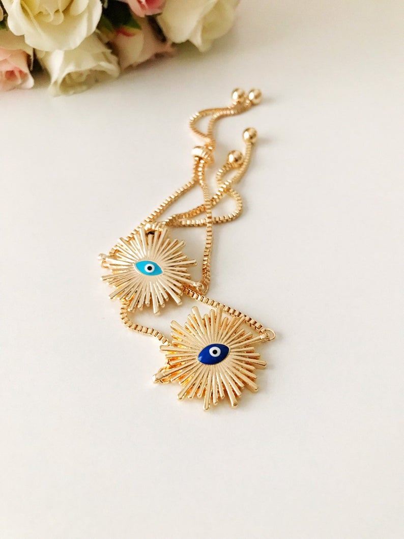 A beautiful Greek Evil Eye Bracelet featuring a sun charm, adjustable gold chain, and a blue evil eye charm, symbolizing protection and good luck.