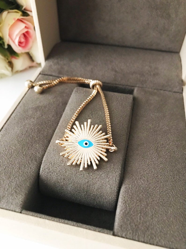 A beautiful Greek Evil Eye Bracelet featuring a sun charm, adjustable gold chain, and a blue evil eye charm, symbolizing protection and good luck.