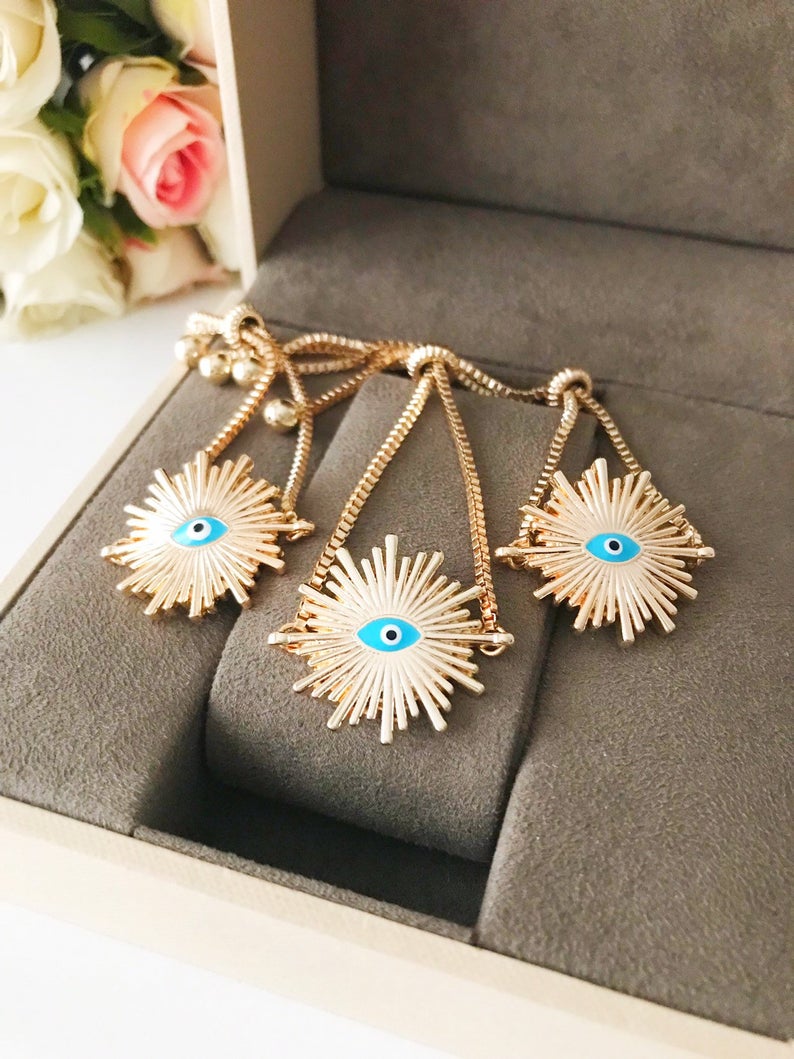 A beautiful Greek Evil Eye Bracelet featuring a sun charm, adjustable gold chain, and a blue evil eye charm, symbolizing protection and good luck.