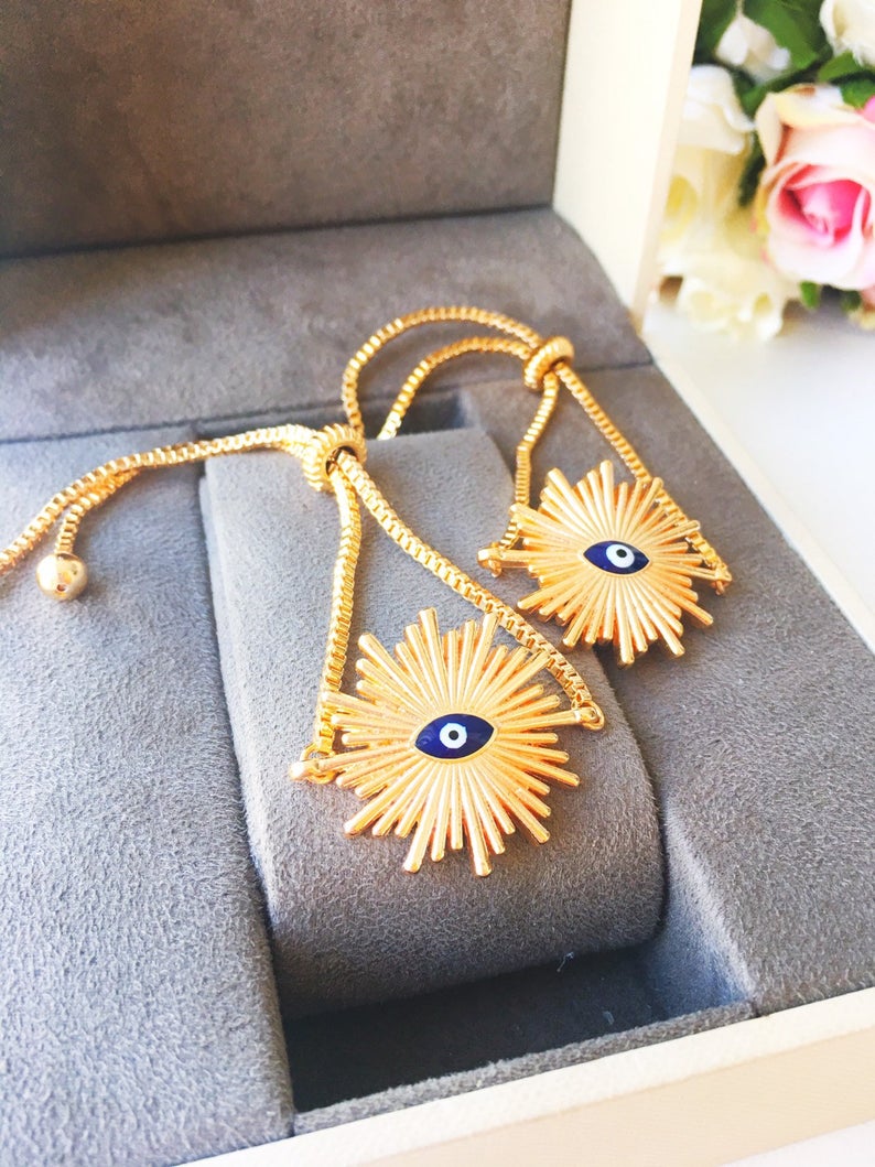 A beautiful Greek Evil Eye Bracelet featuring a sun charm, adjustable gold chain, and a blue evil eye charm, symbolizing protection and good luck.
