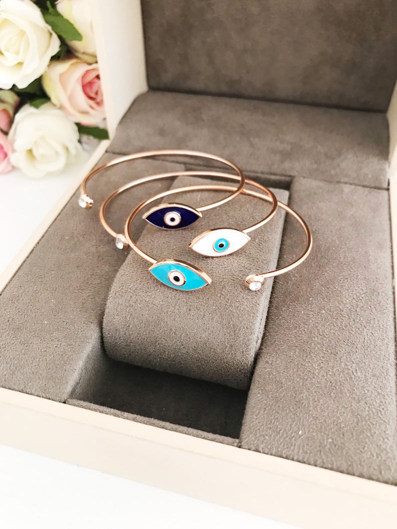Greek Evil Eye Bracelet featuring a movable blue evil eye bead on a stainless steel bangle, available in multiple colors.