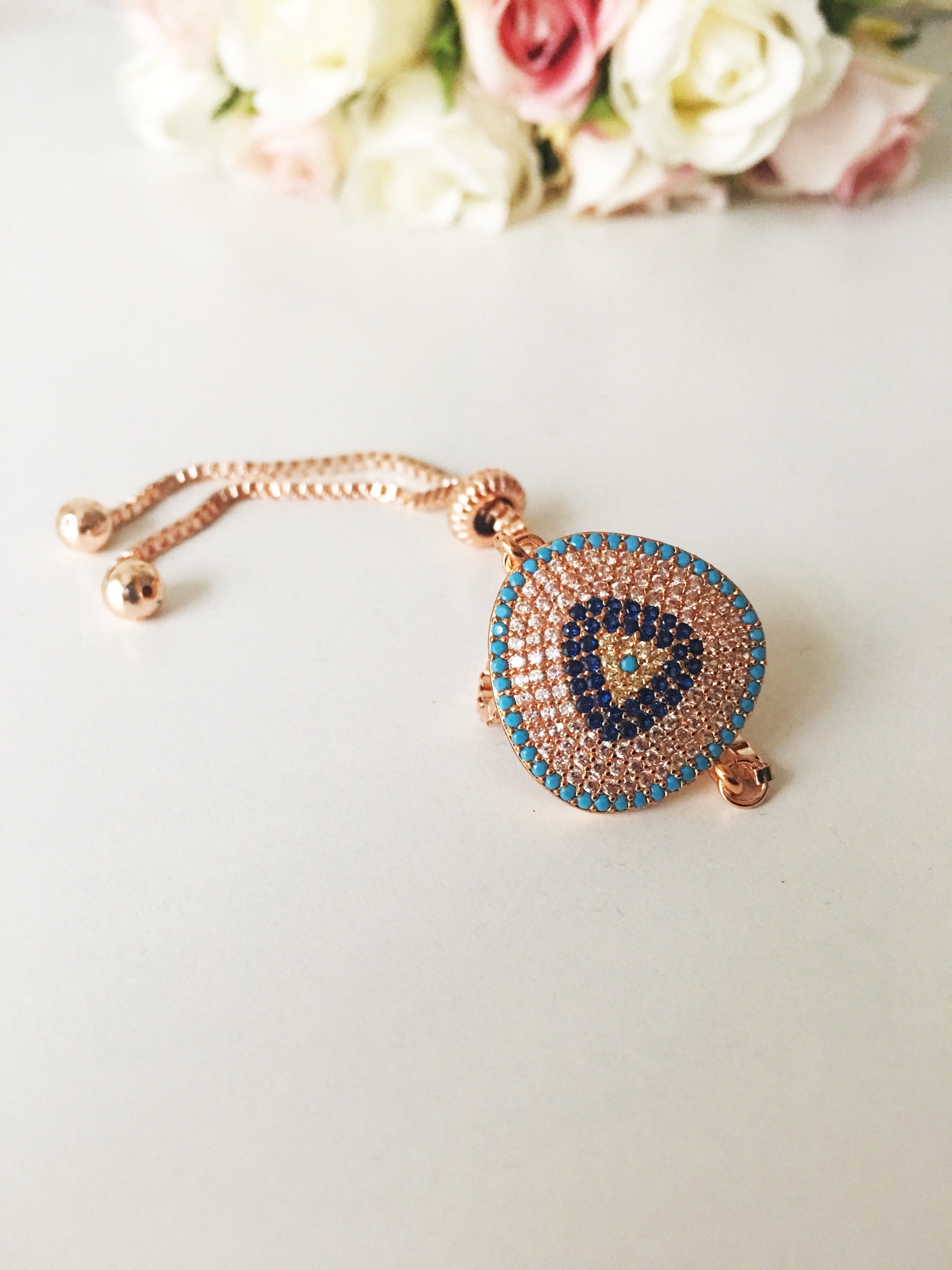 A collection of Greek Evil Eye Bracelets in silver, gold, and rose gold finishes, featuring sparkling zirconia charms on adjustable stainless steel bands.