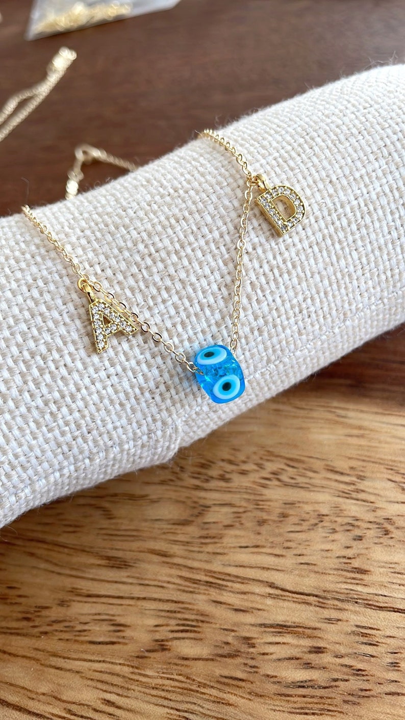 A beautiful Greek Evil Eye Necklace featuring a blue glass bead and 14K gold chain with customizable initials.