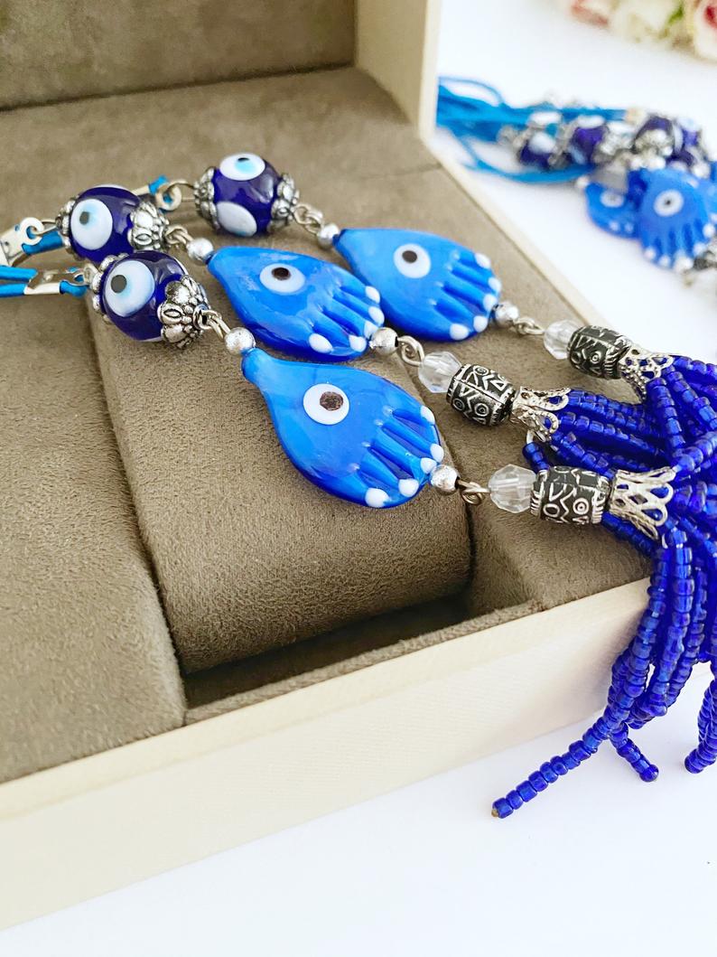 A beautifully crafted Hamsa hand evil eye car mirror charm featuring blue glass beads and a stylish tassel, perfect for car decor.