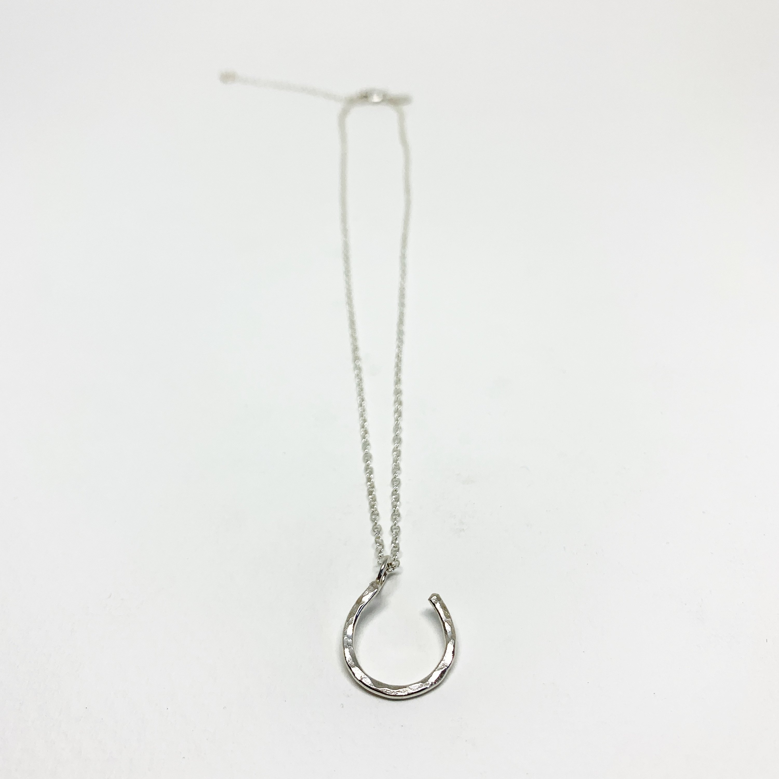 A delicate Hanging Lucky Horseshoe Charm Necklace featuring a hammered horseshoe pendant in sterling silver, yellow gold fill, or rose gold fill.