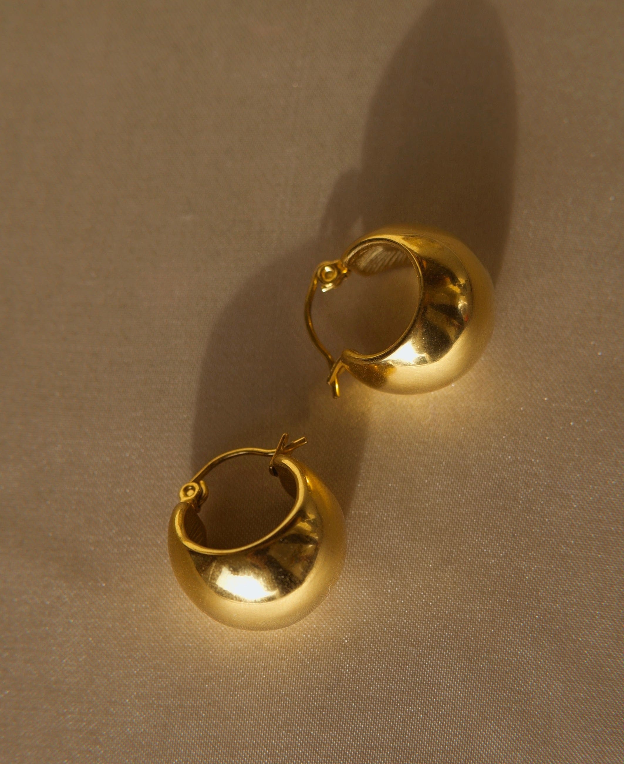 A pair of Hazel ball hoop earrings made from stainless steel with 18Kt yellow gold PVD plating, showcasing a unique and bold design.