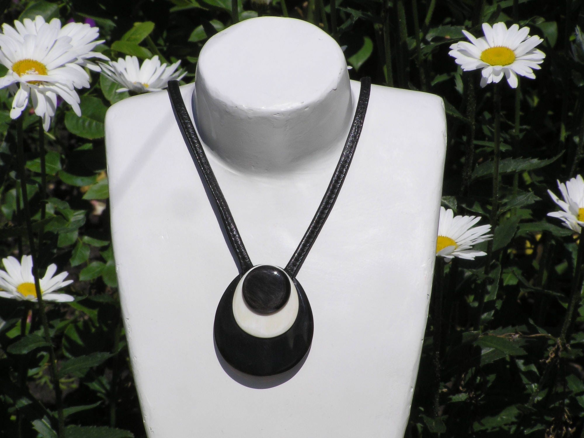 Handmade drop-shaped horn pendant on a leather cord, showcasing unique black and white patterns.