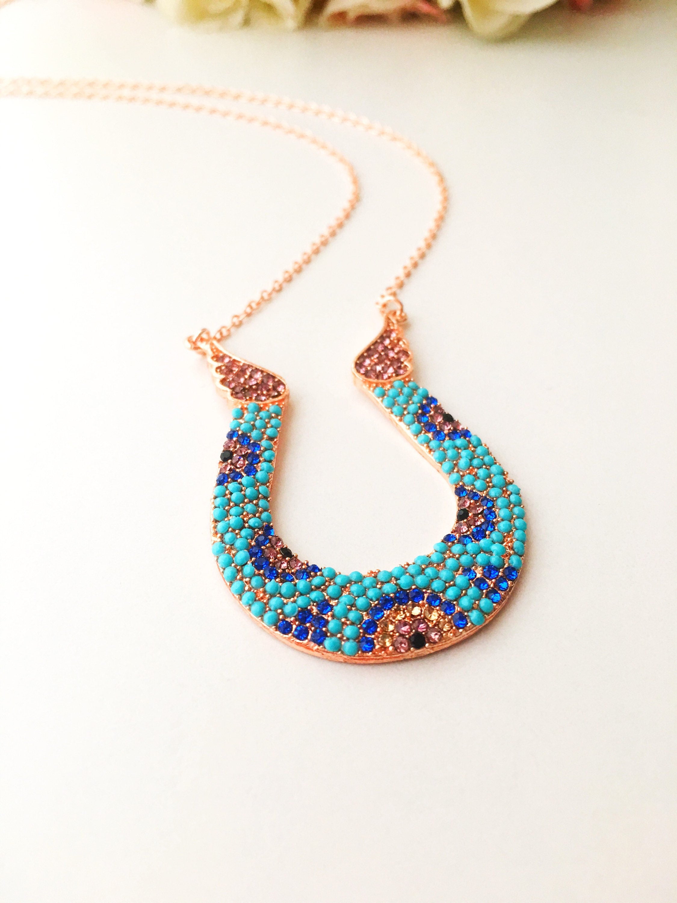 Handmade turquoise horseshoe necklace with colorful zirconia and rose gold chain, featuring an evil eye charm.