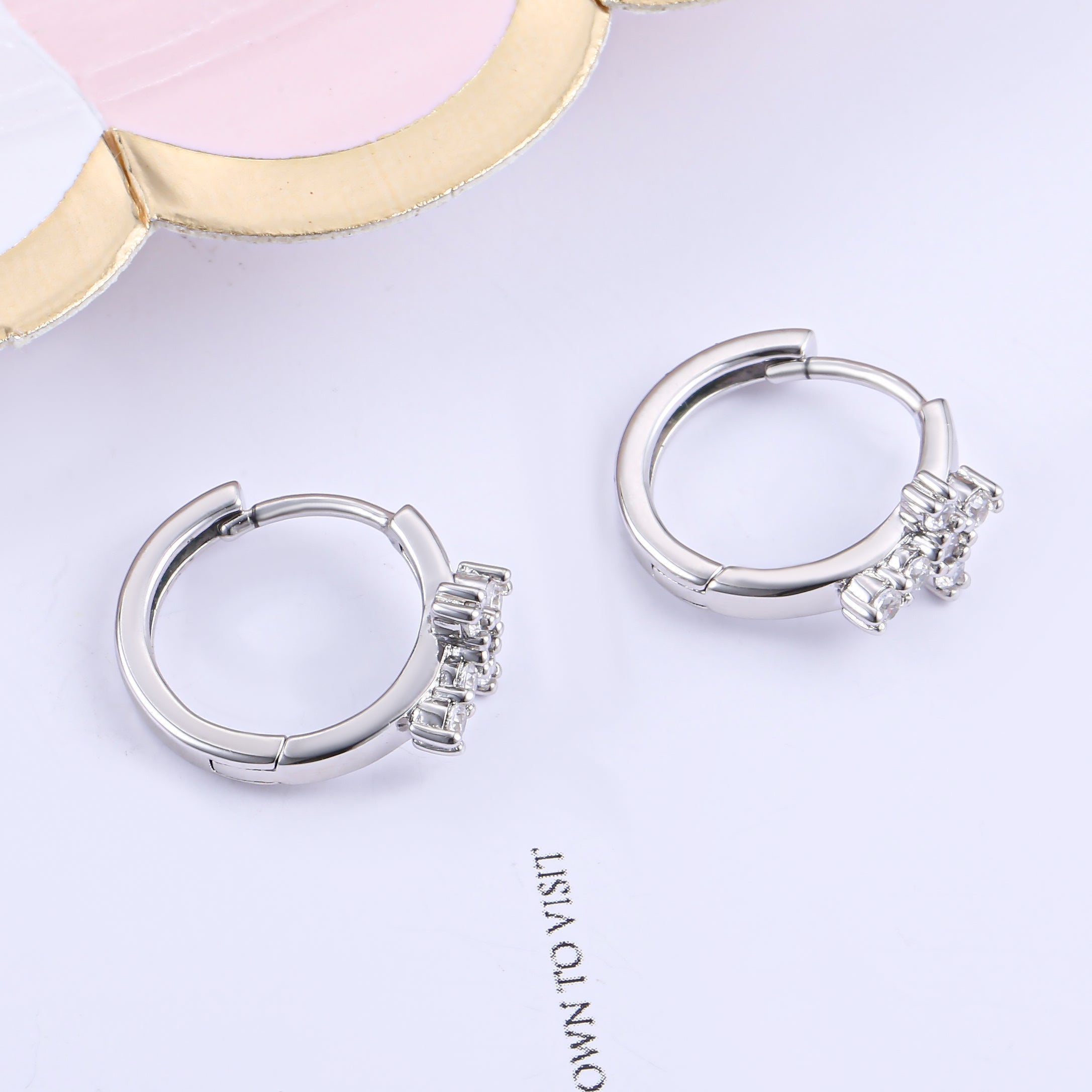 A pair of Huggie hoop cross earrings made from 925 sterling silver with white gold finish and white sapphire stones.