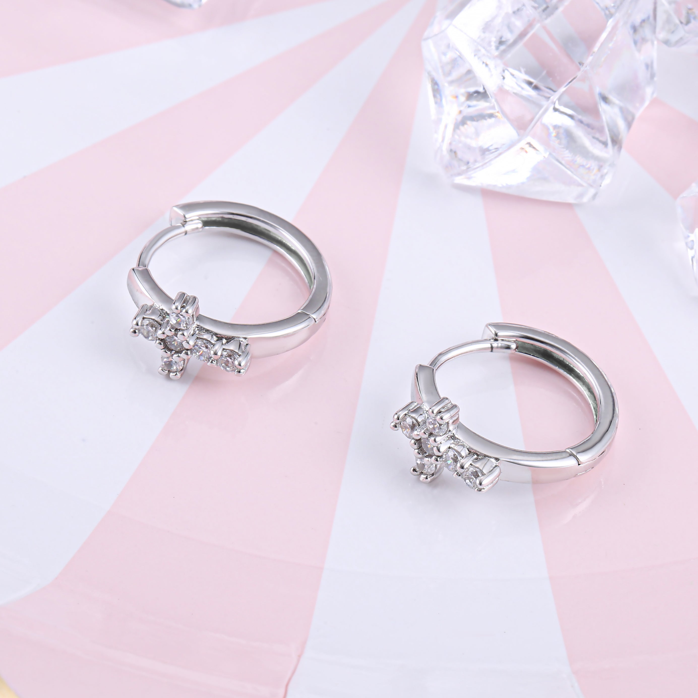 A pair of Huggie hoop cross earrings made from 925 sterling silver with white gold finish and white sapphire stones.