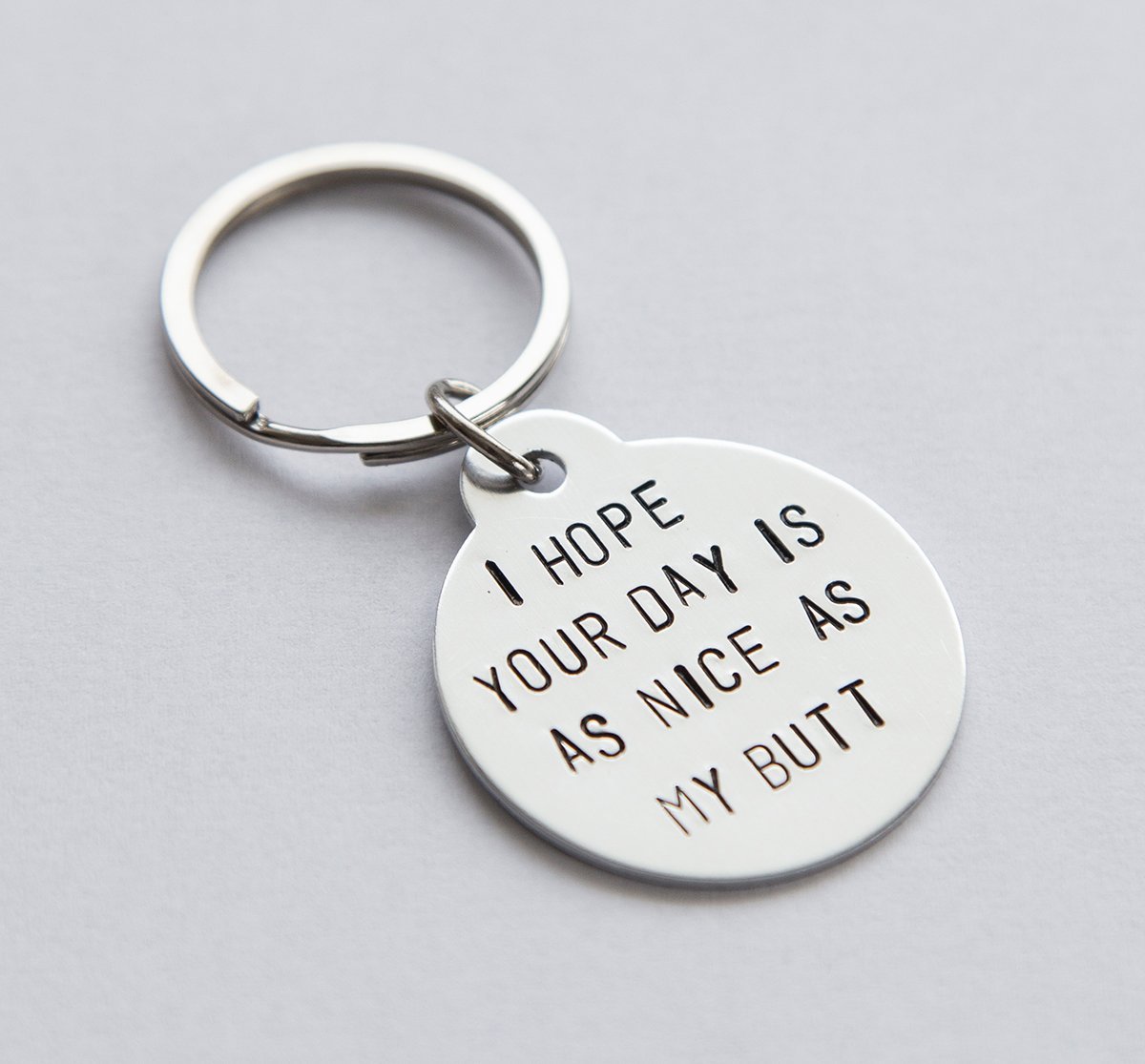 A humorous keyring with the phrase 'I hope your day is as nice as my butt', featuring a stainless steel keyring and lightweight aluminum tag.